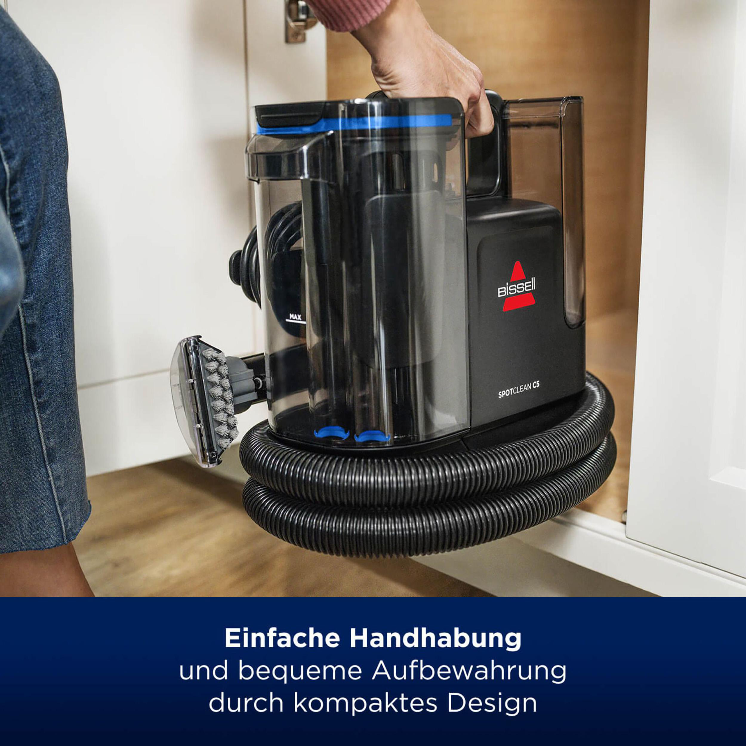 Eine Person hält einen schwarz-blauen Bissell SpotClean C5 Staubsauger.