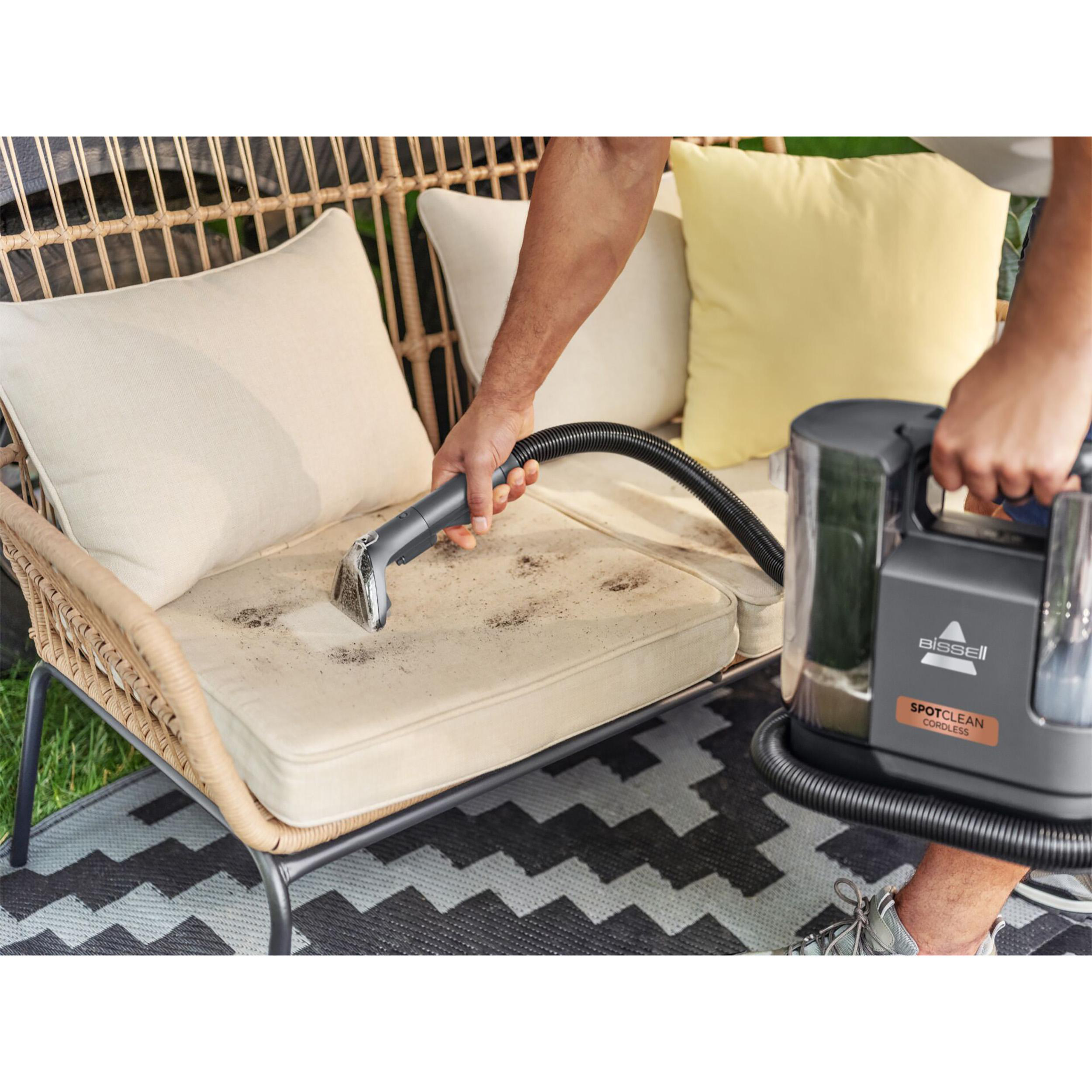 Eine Person reinigt mit einem Bissell SpotClean Cordless-Staubsauger ein schmutziges Outdoor-Kissen.