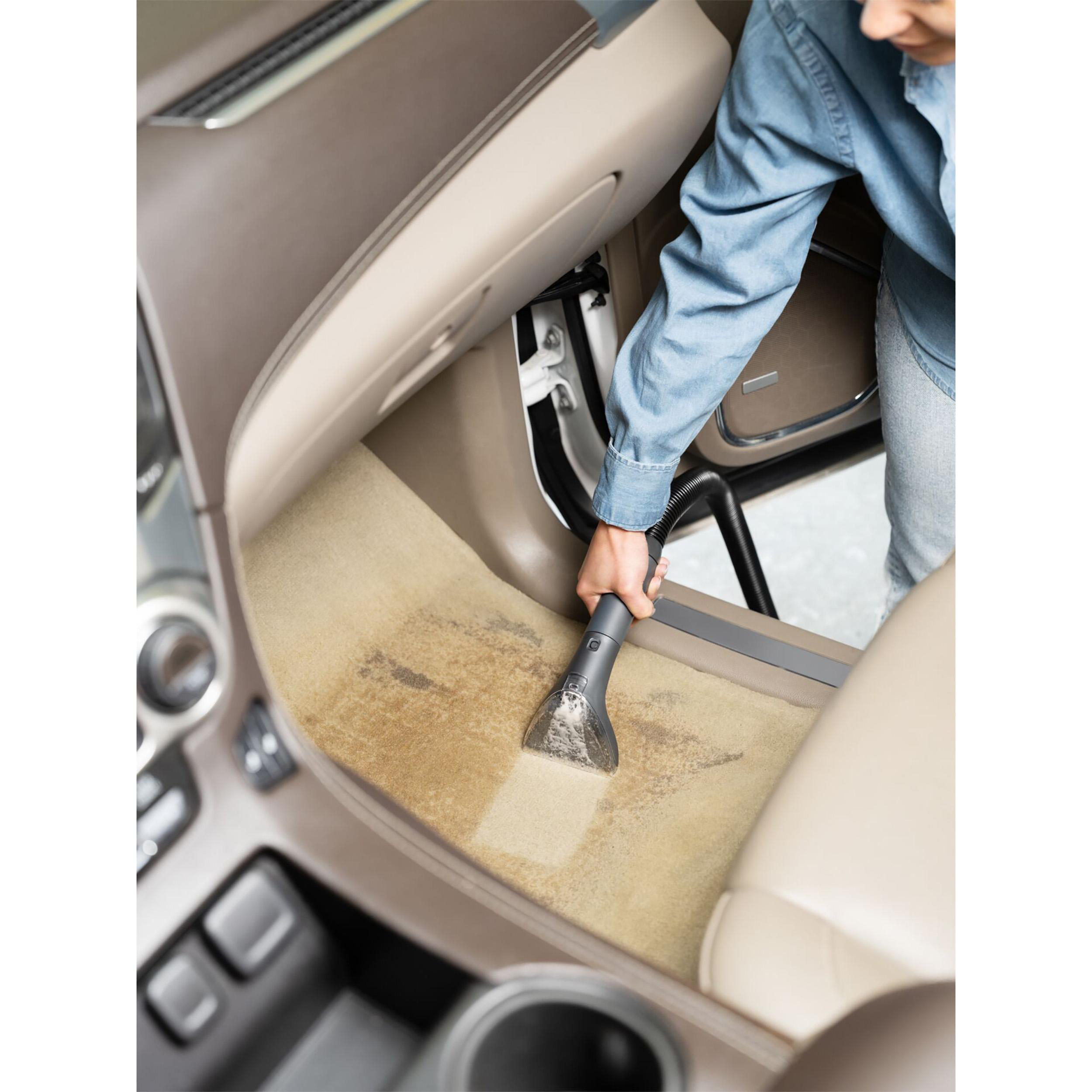 Eine Person saugt den beigefarbenen Teppich eines Autos.