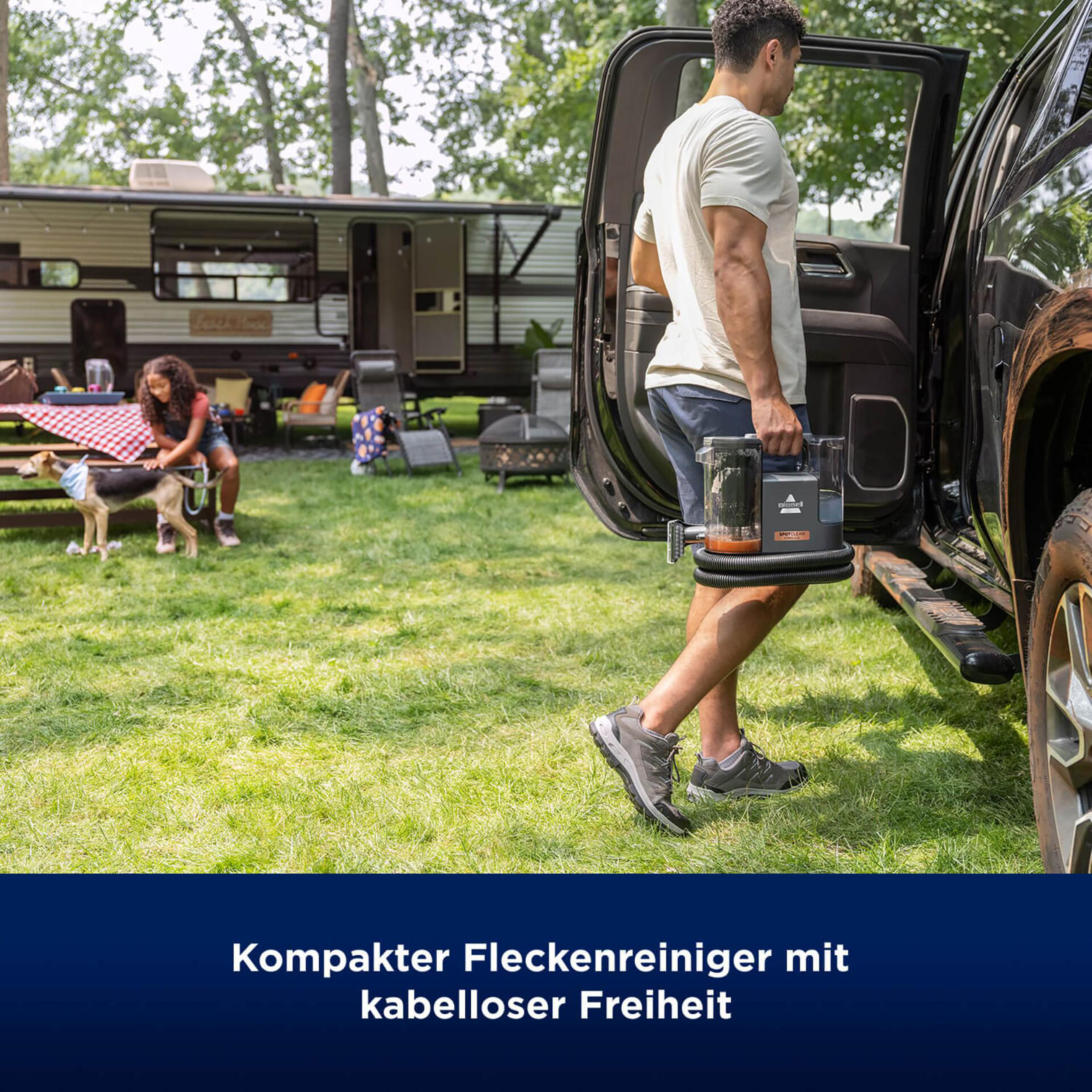 Mann, der einen SpotClean C5 Staubsauger im Freien in der Nähe eines Wohnwagens und Hundes trägt.