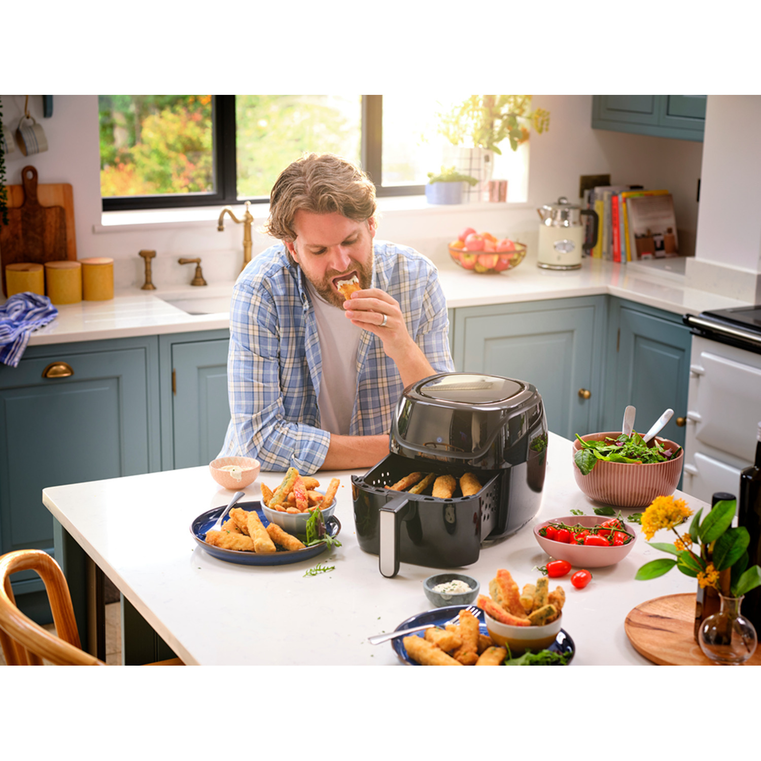 Man eet gefrituurd voedsel van een bord, airfryer en ander voedsel op tafel.