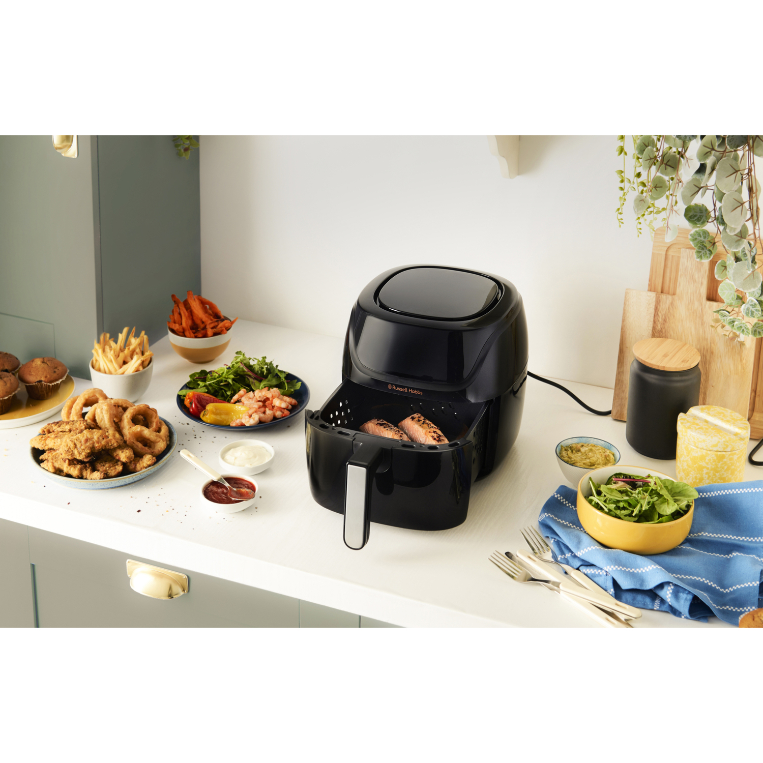 Airfryer met eten, waaronder uienringen en friet, op een aanrecht.
