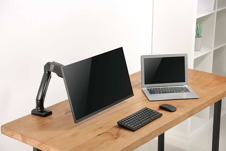 Irodai beállítás: monitor, laptop, billentyűzet és egér egy fa asztalon.