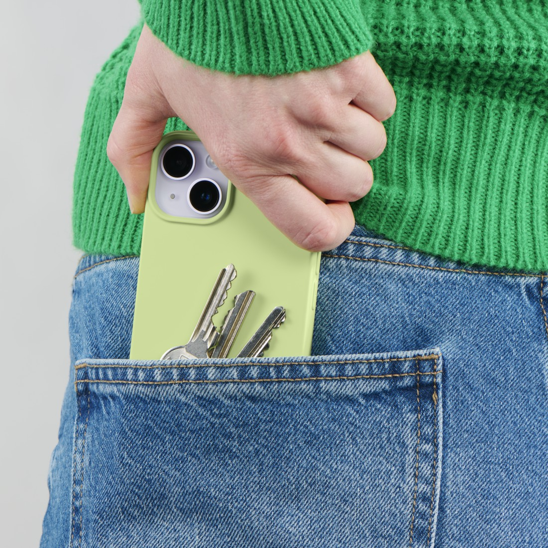 Die Hand einer Person, die ein Telefon in eine Jeanstasche steckt. Schlüssel sind in der Tasche mit dem Telefon sichtbar.