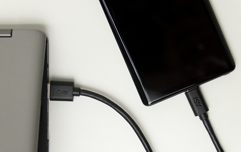 Egy fekete USB-C kábel egy ezüst laptopot és egy fekete okostelefont köt össze.