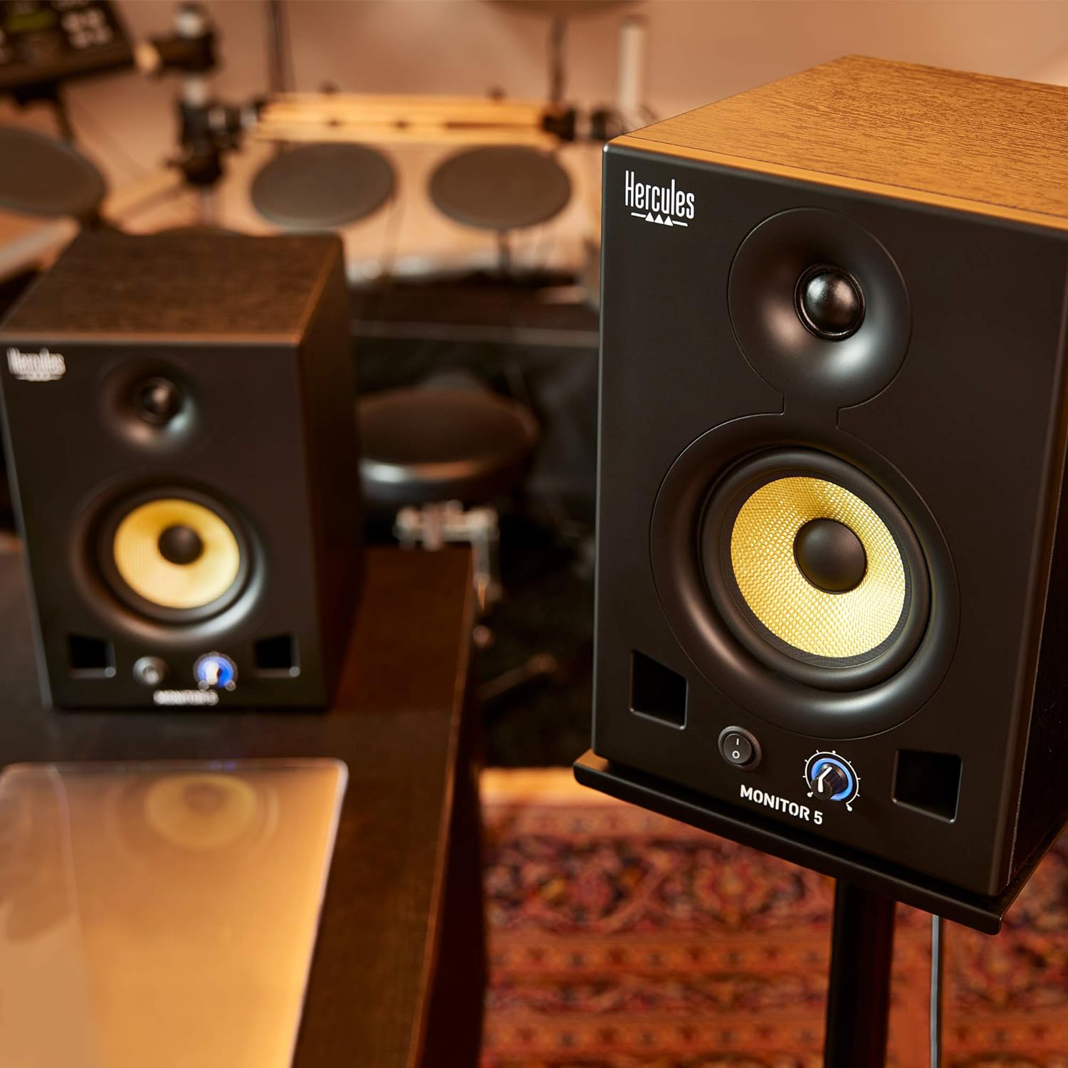 Due altoparlanti neri Hercules Monitor 5 con coni gialli su supporti in un ambiente studio.