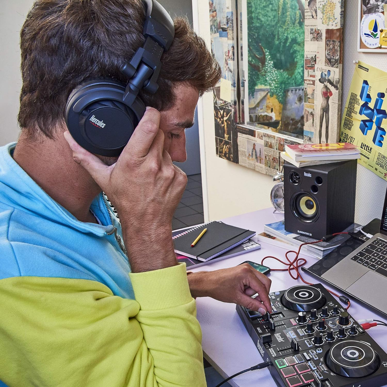 Uomo con cuffie, usa un mixer da DJ. C'è un altoparlante, quaderni e altri oggetti.