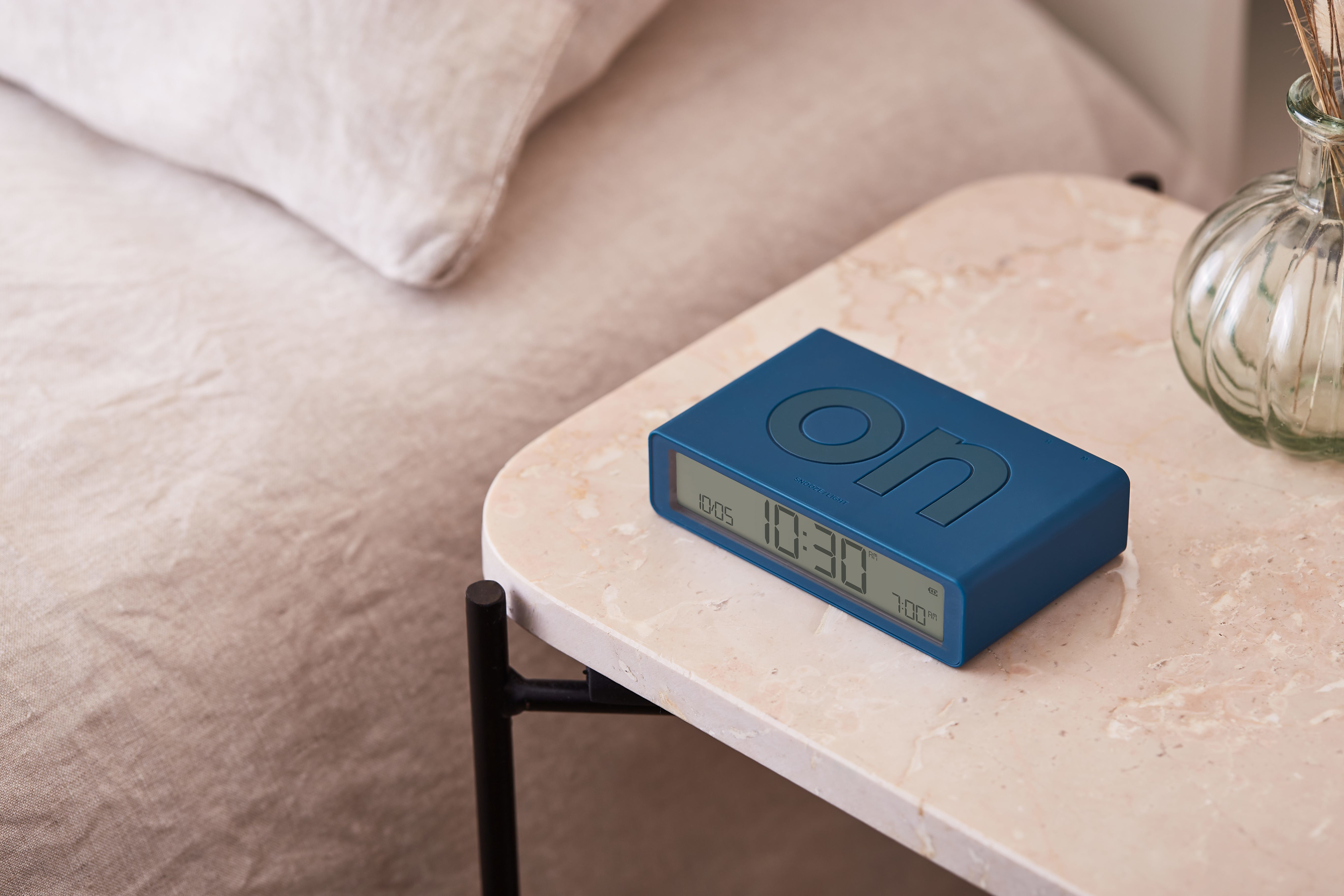 Sveglia blu su un tavolo di marmo, che mostra l'ora e la parola 'ON', accanto a un letto.