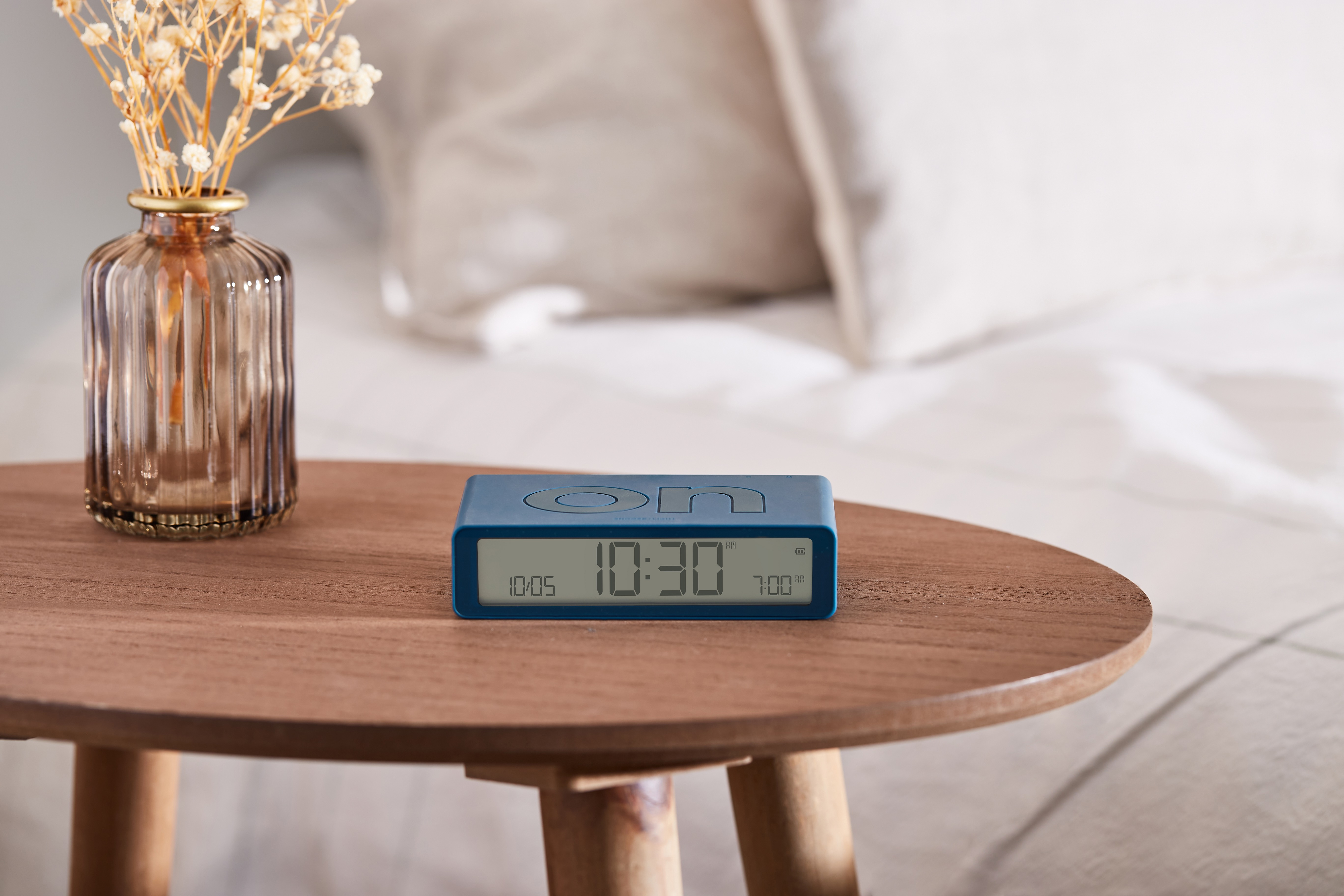 Sveglia blu su un tavolo di legno. L'ora è 10:30. Vaso con fiori sullo sfondo.