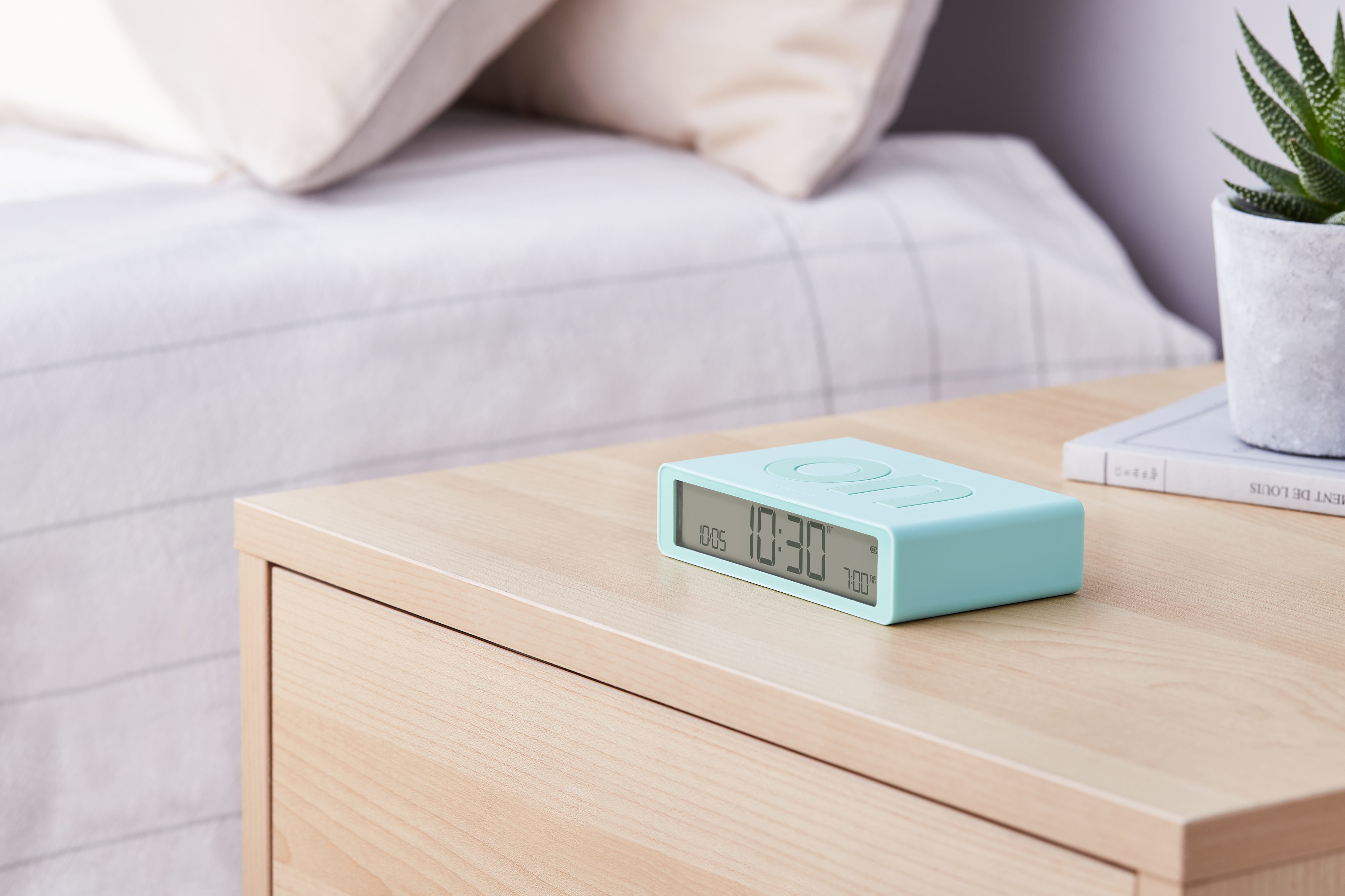 Una sveglia turchese su un comodino accanto a un letto con cuscini.