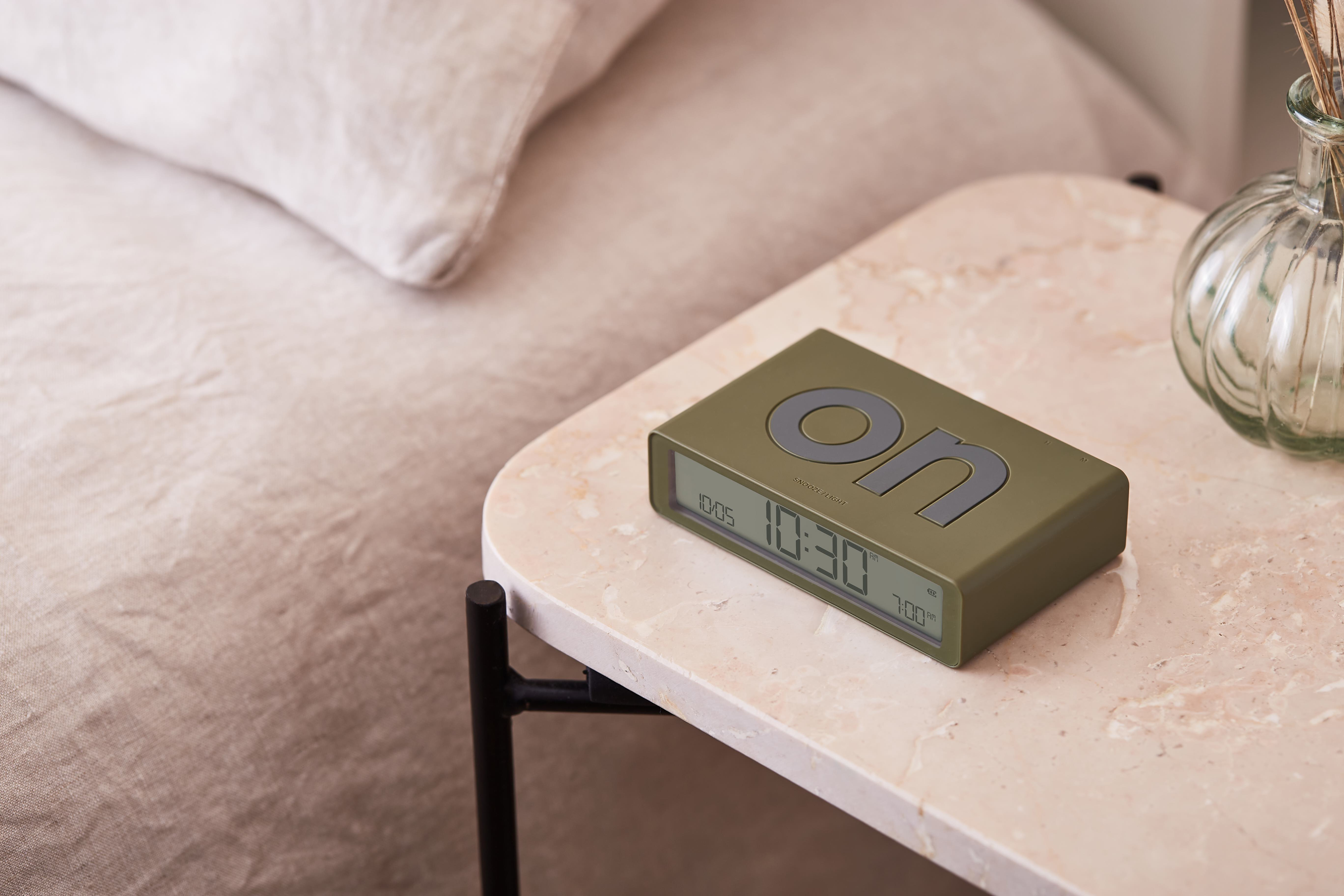 Una sveglia digitale verde oliva su un tavolo di marmo segna le 10:30. È visibile la parola 'on'.