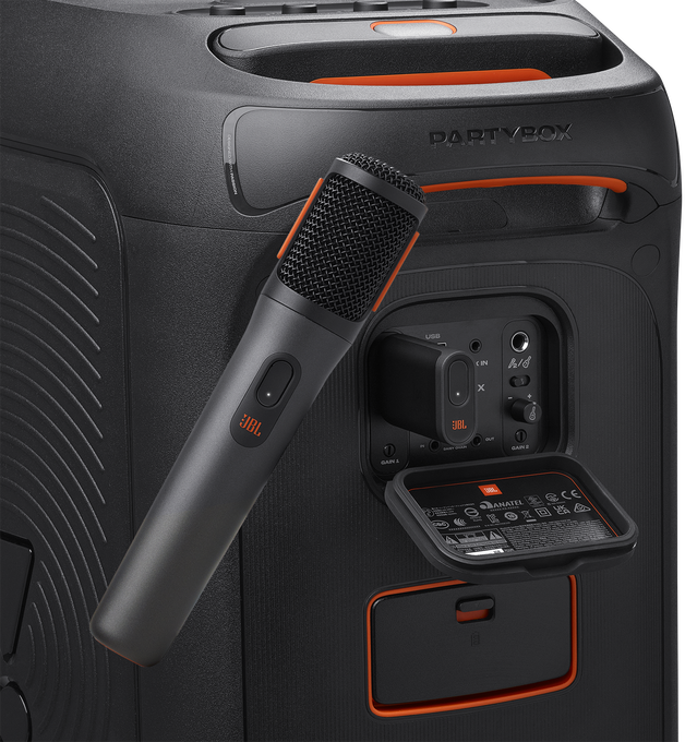 Fekete JBL Partybox hangszóró mikrofonnal. A mikrofont a vezérlőpanel közelében tartják.