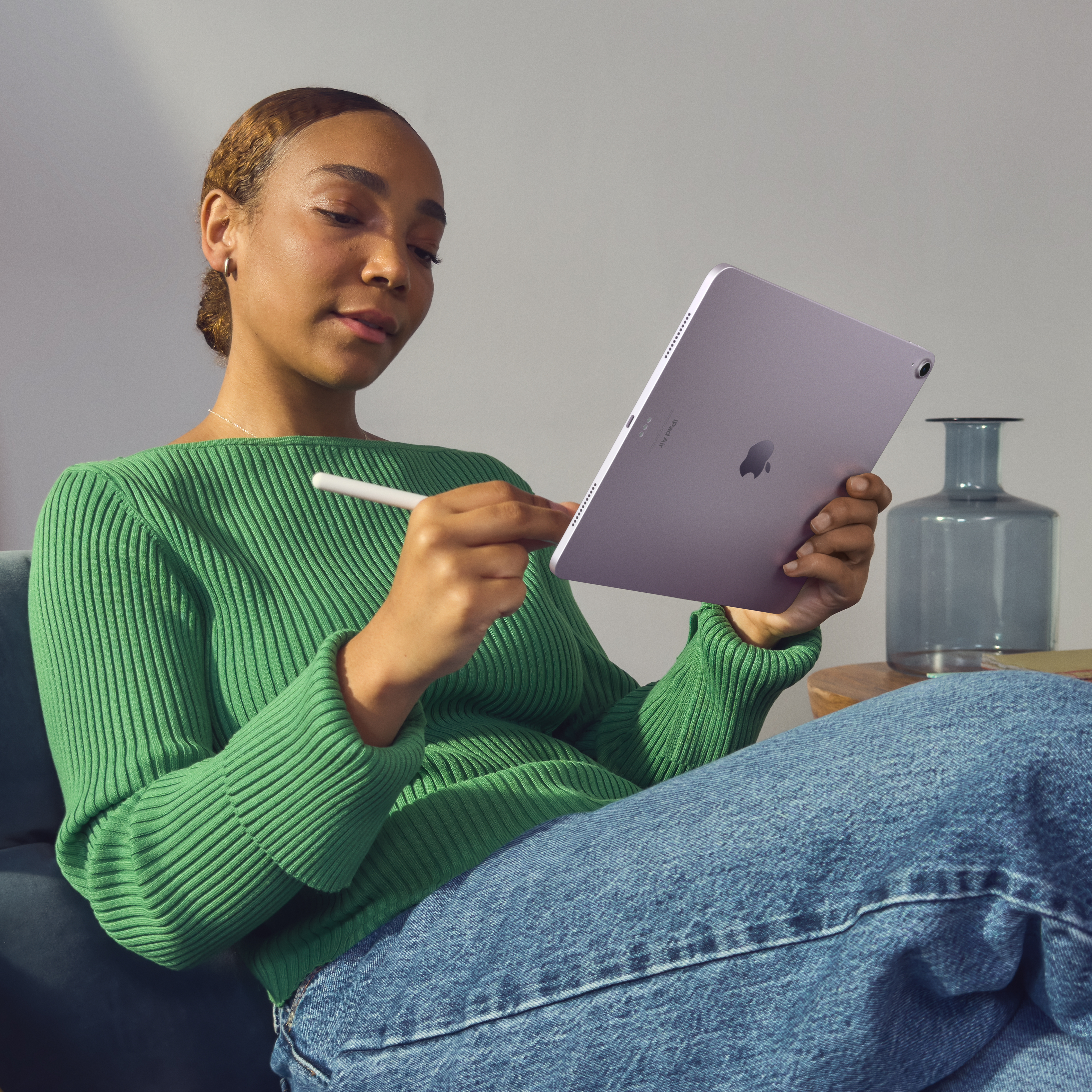 Yeşil kazaklı, mor iPad ve kalem tutan bir kadın.