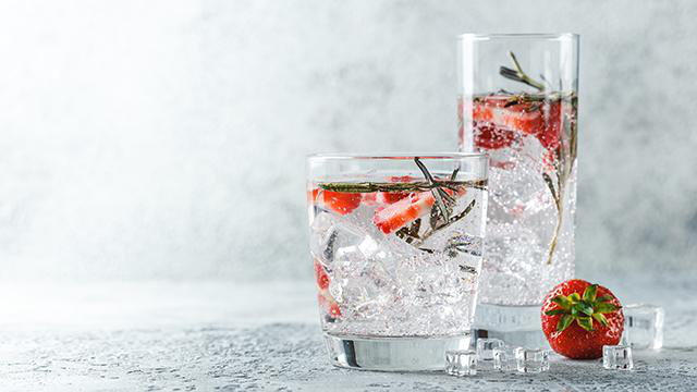 Zwei Gläser Cocktails mit Erdbeeren und Rosmarin, Eiswürfeln und eine Erdbeere.