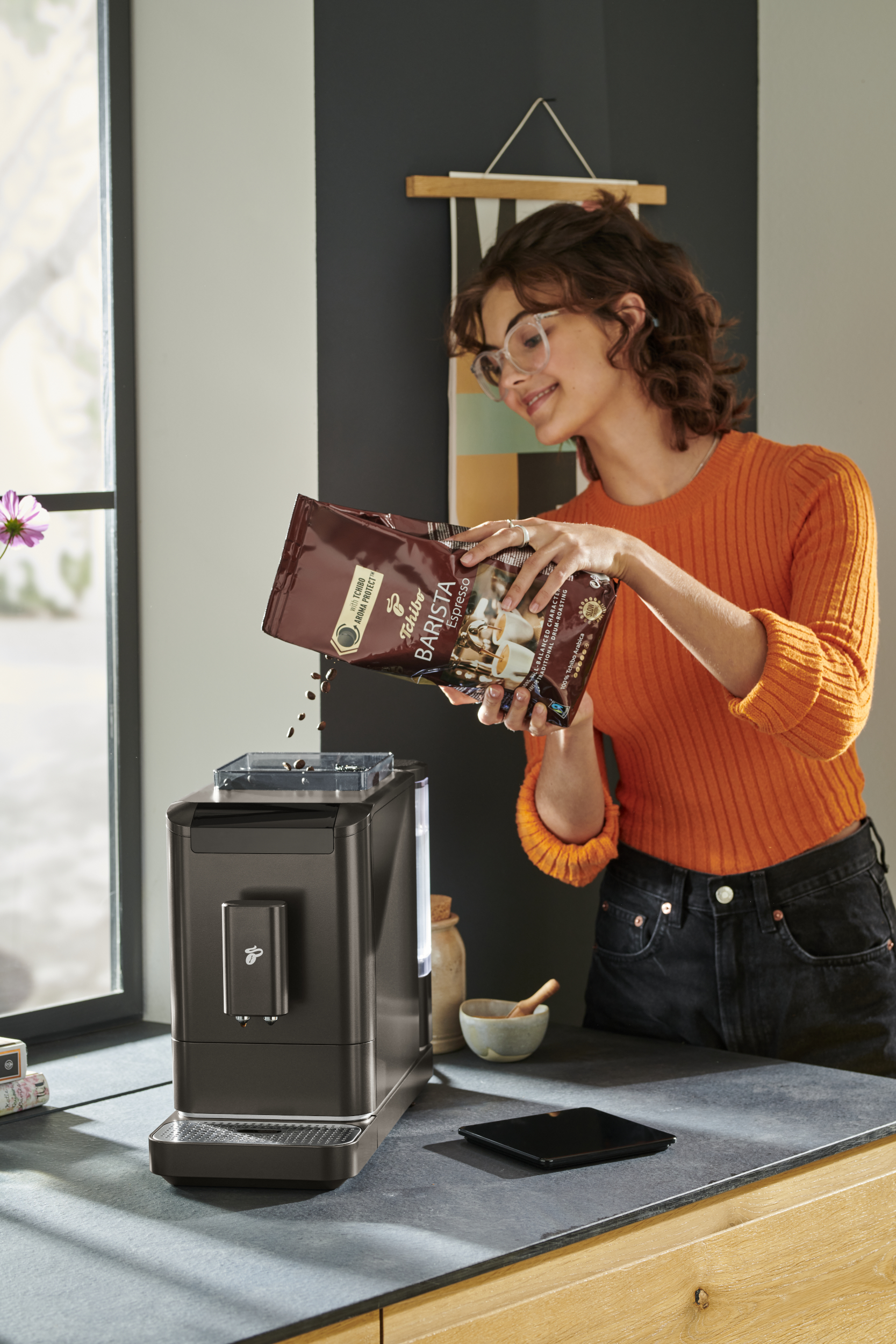 Kobieta wsypuje ziarna kawy do ekspresu do kawy, w otoczeniu kuchni.