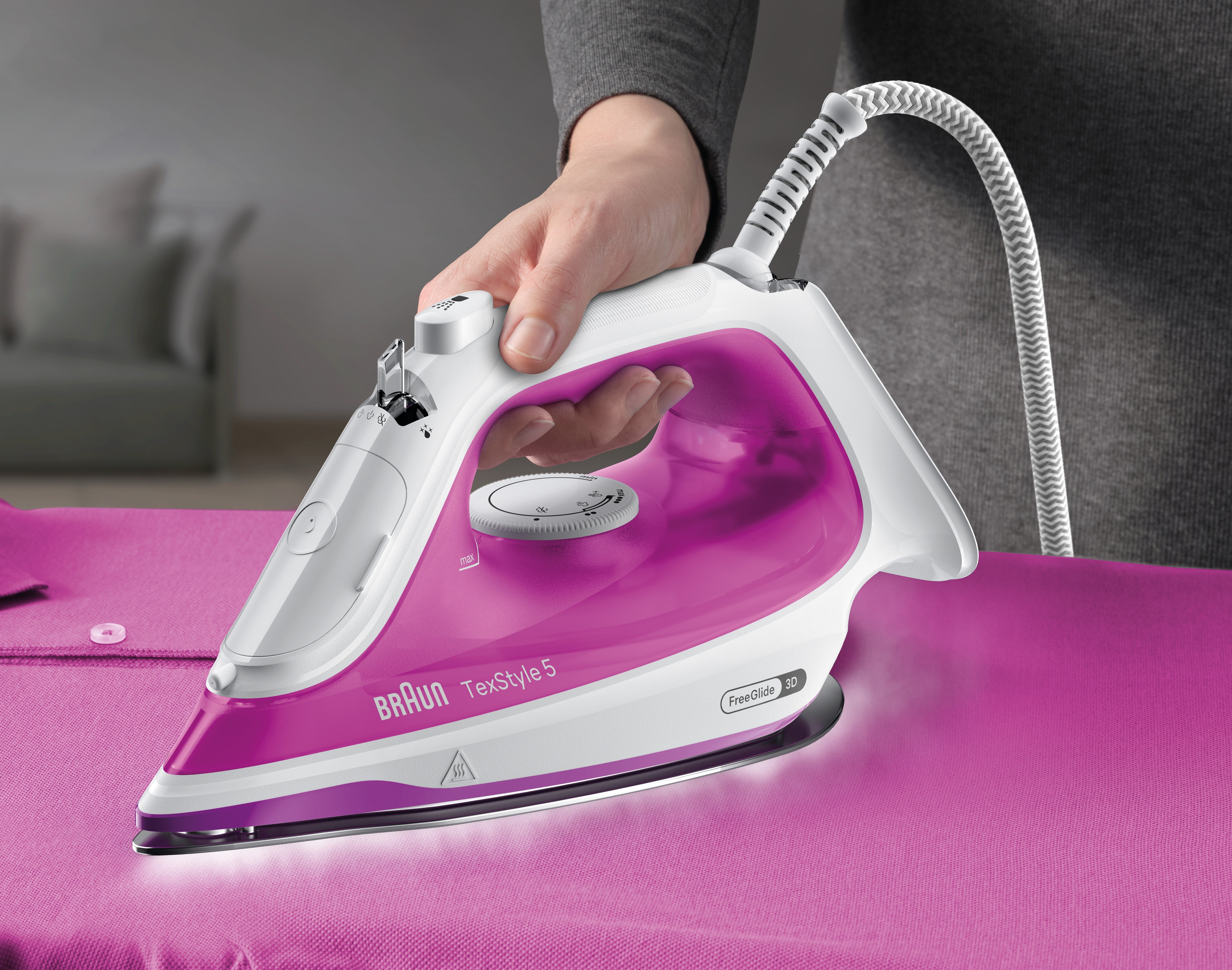 Ein rosa und weißes Bügeleisen bügelt ein rosa Hemd auf einem Bügelbrett.
