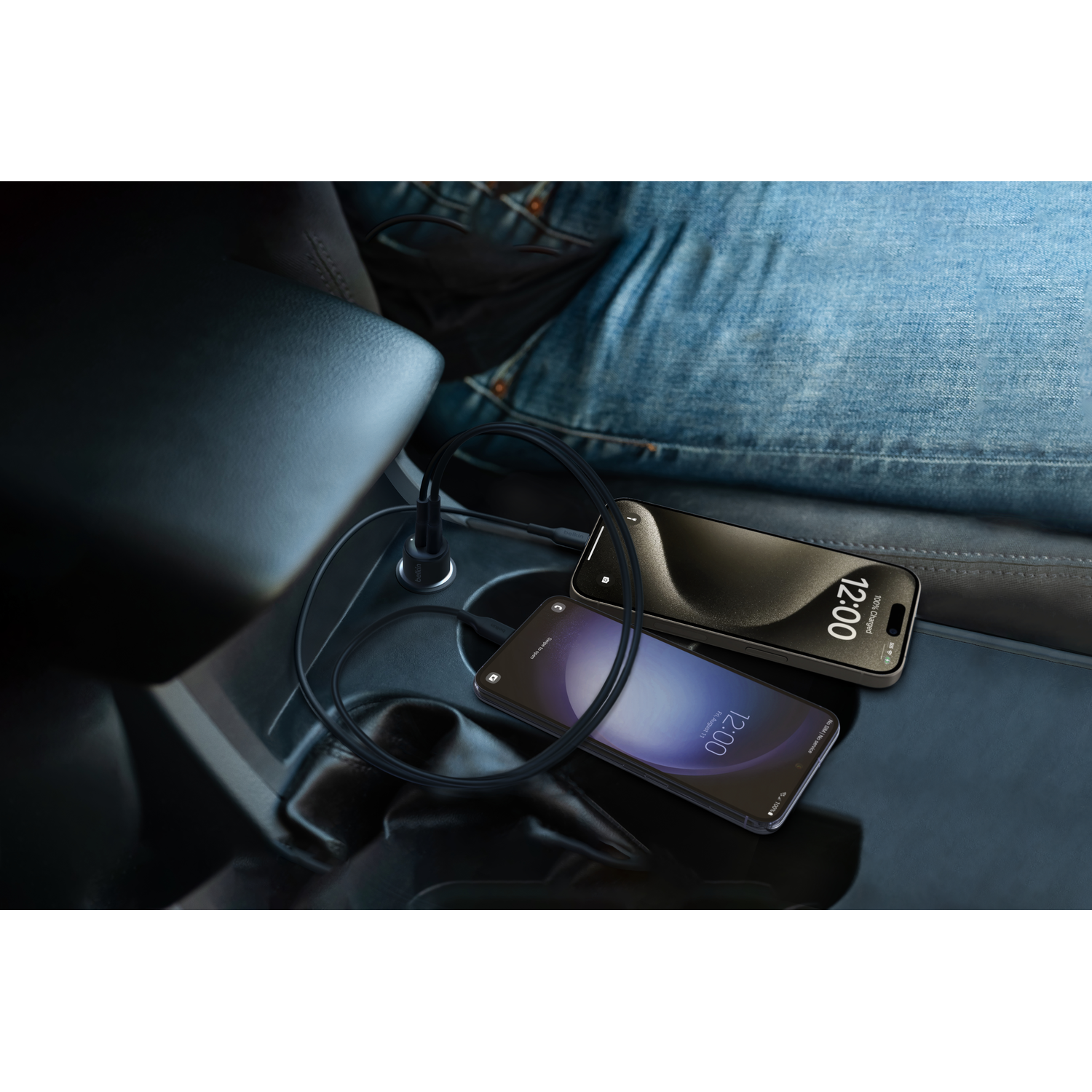 Two phones charging, one on a car console, the other on lap.  A charging cable is visible.