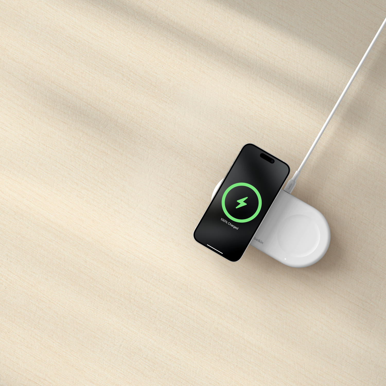 Phone charging on a white wireless charger on a light brown wood surface.