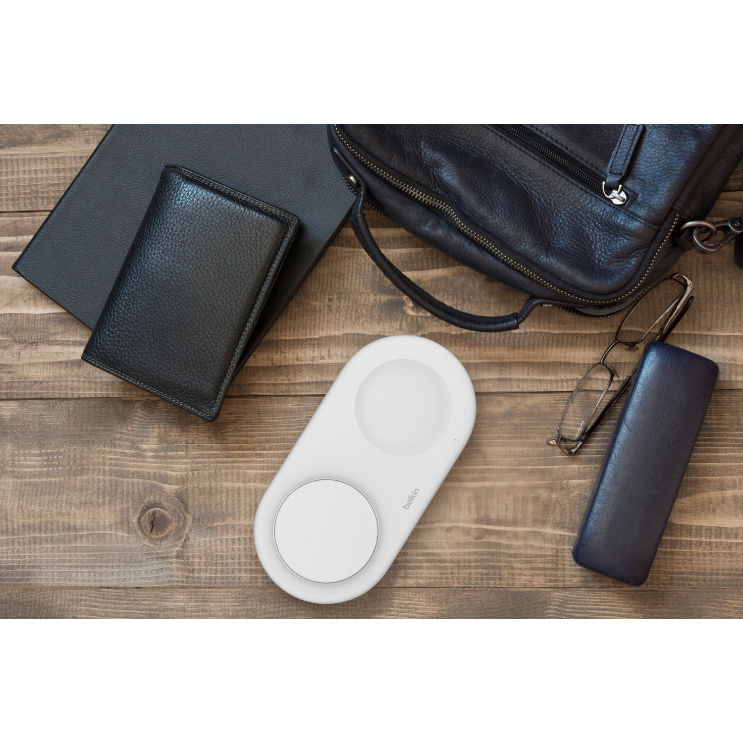 White wireless charging pad, wallet, glasses, and a bag on a wooden table.