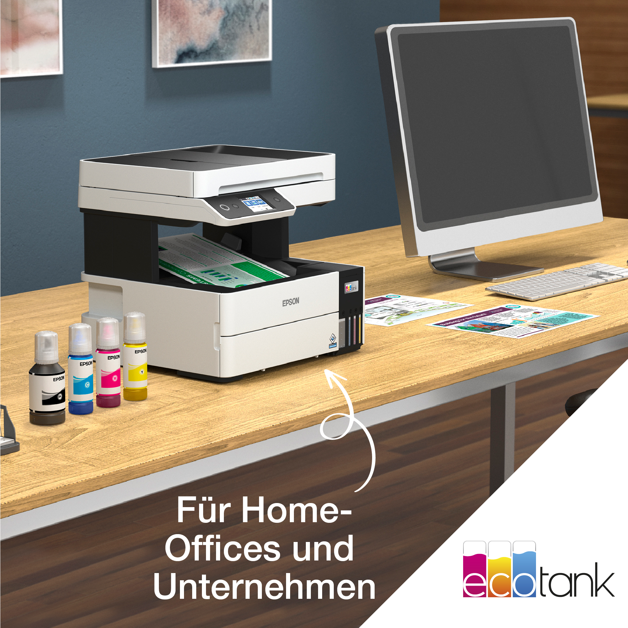Drucker mit Tintenflaschen auf einem Holztisch. Ein Computermonitor rechts. Text auf dem Tisch.