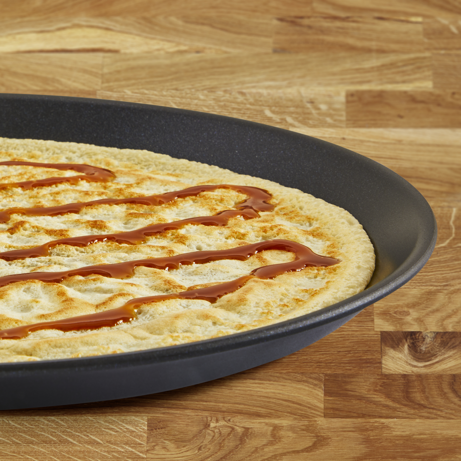 Naleśnik na czarnej patelni, polany sosem karmelowym. Drewniany stół.