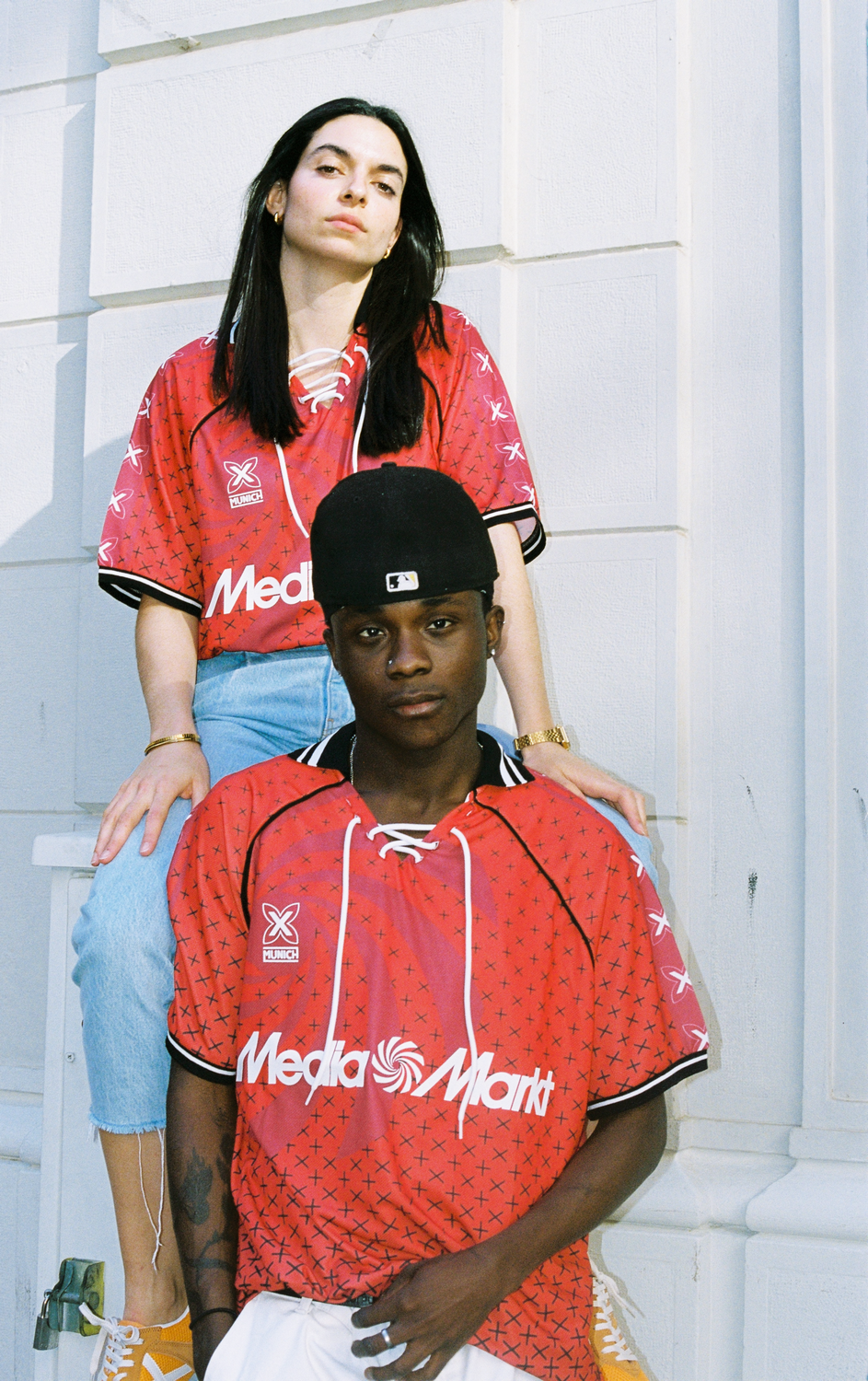 Dos personas con camisas rojas y blancas con el logo 'Media Markt', de pie afuera.