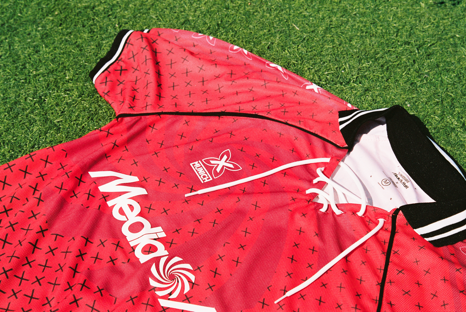 Una camiseta de fútbol roja con detalles blancos y logos, sobre hierba verde.
