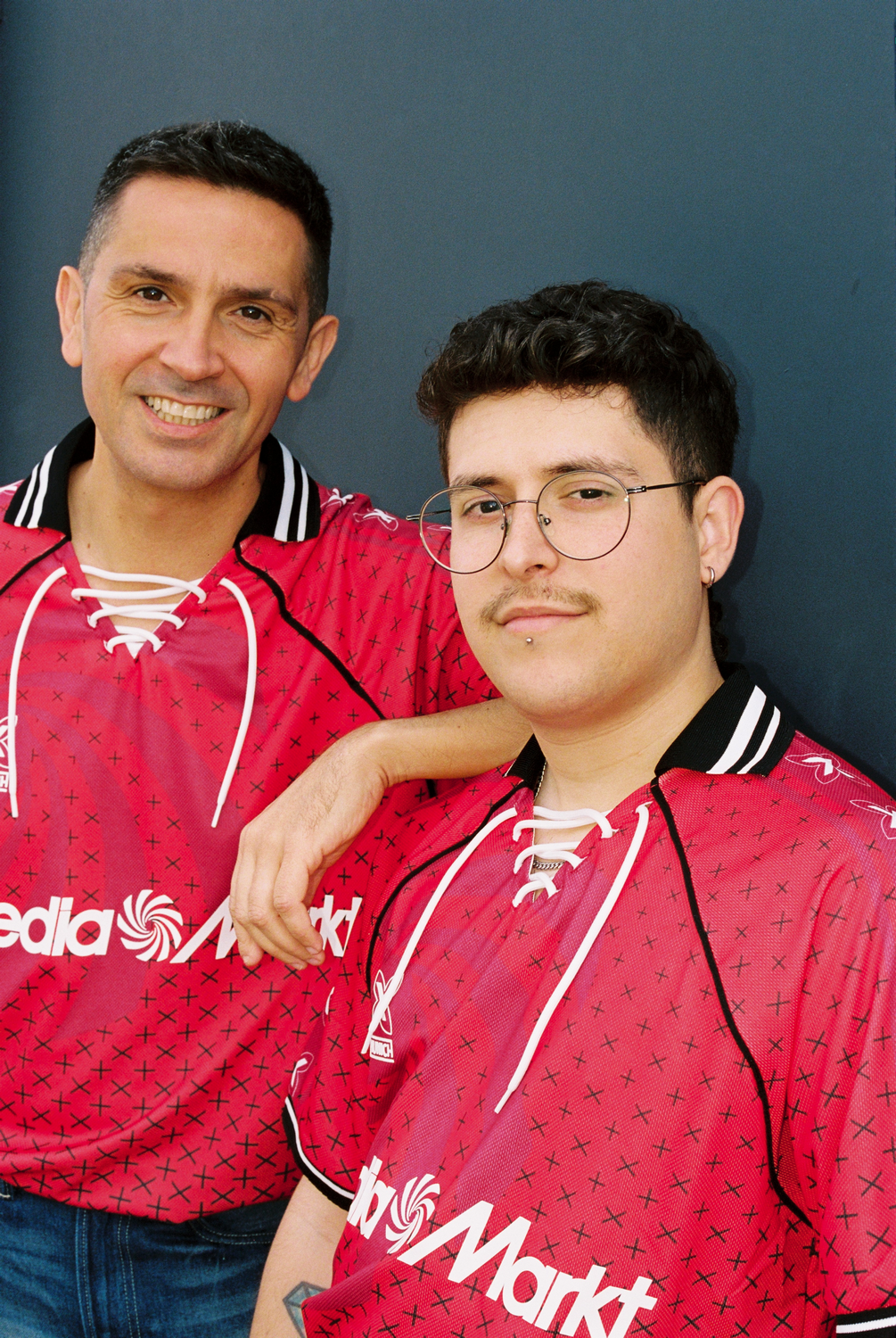 Dos hombres con camisas rojas a juego con un logo, sonriendo a la cámara.