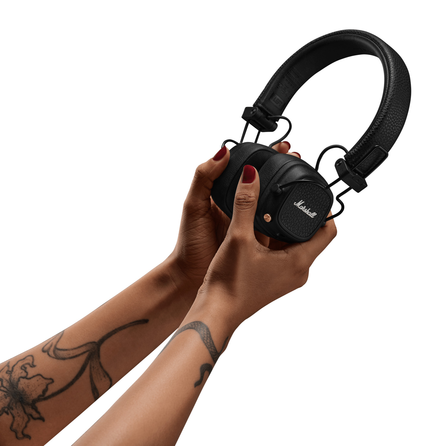 Mains tenant un casque Marshall noir. La personne a des tatouages. Fond blanc.