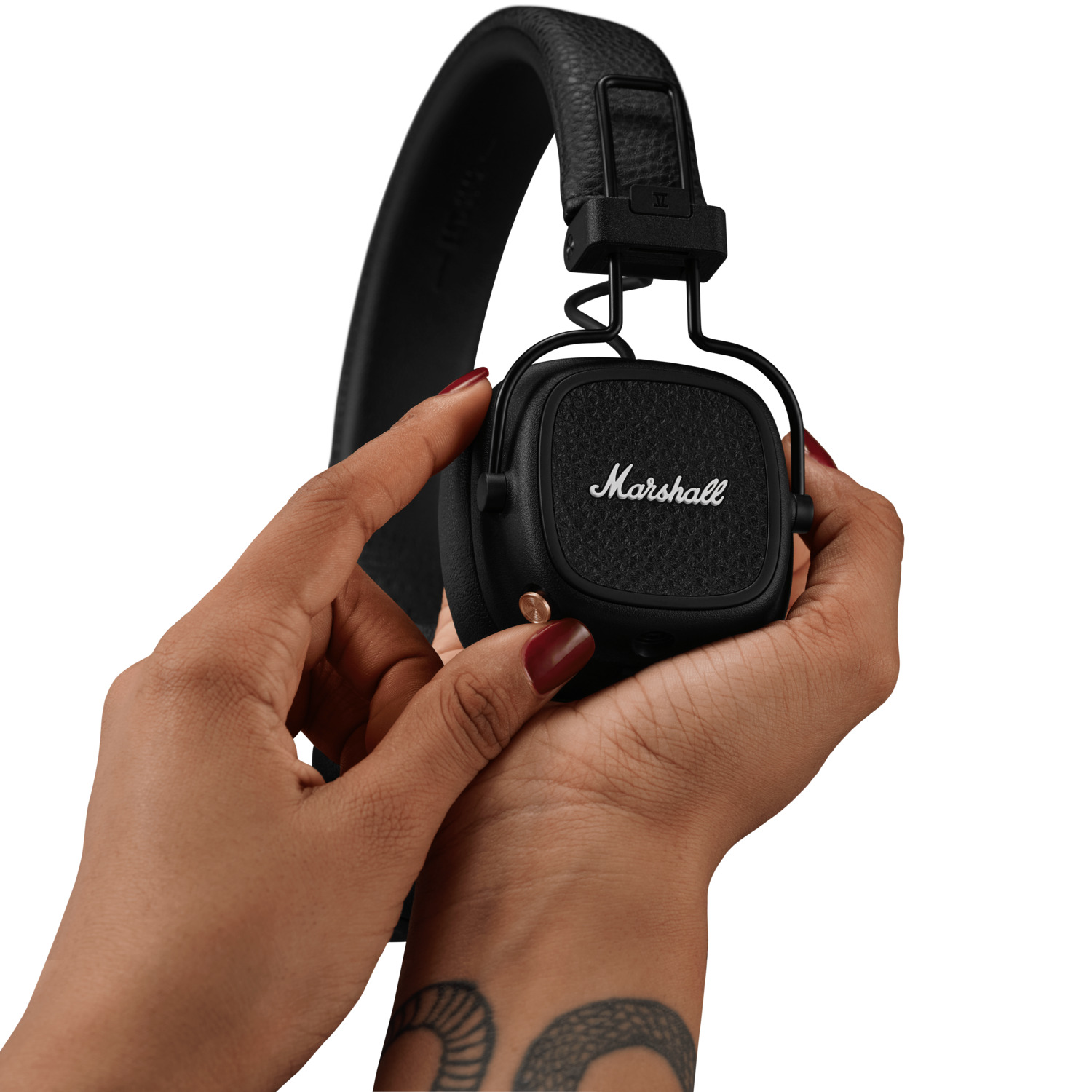 Mains tenant un casque Marshall noir. La main gauche ajuste l'écouteur, vernis à ongles rouge.