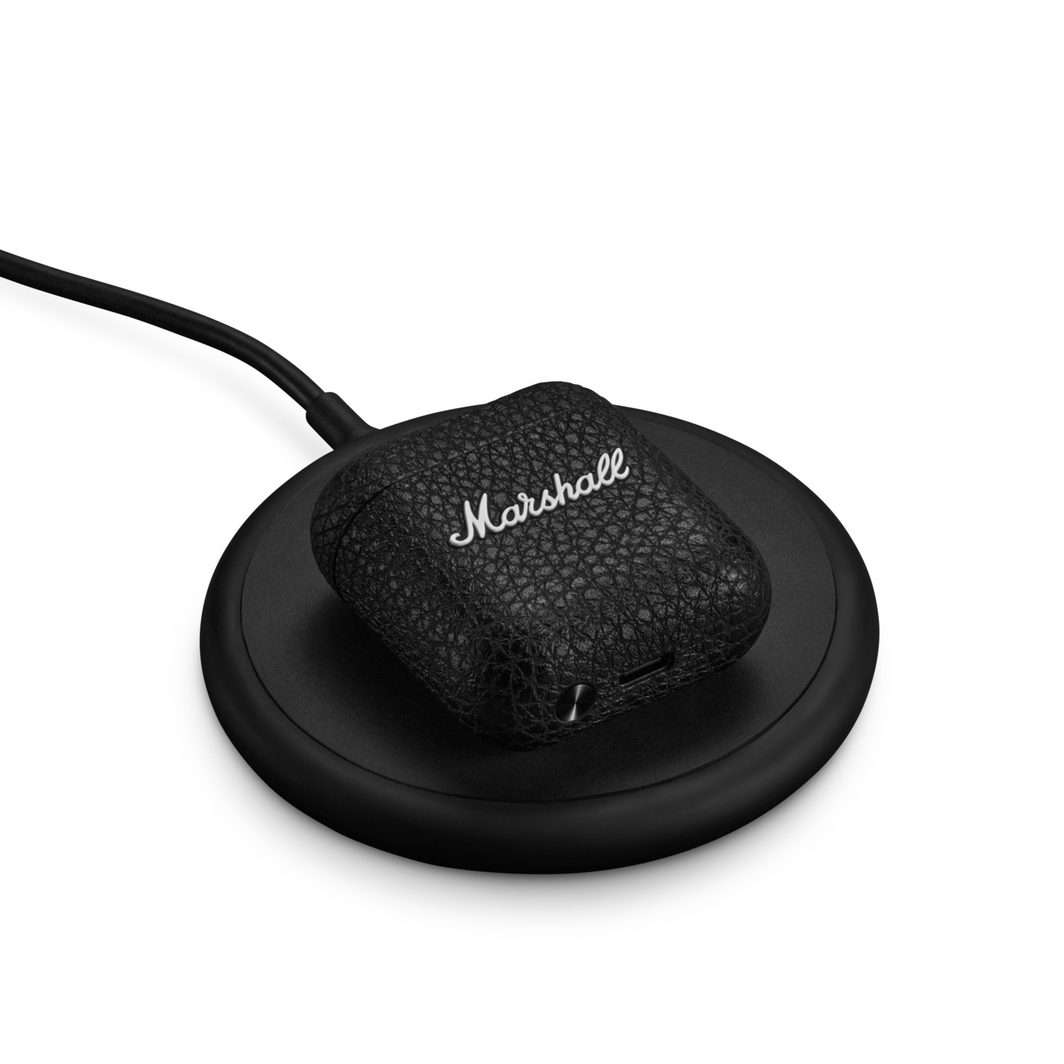Écouteurs Marshall noirs se chargeant sur un chargeur sans fil sur une surface blanche.