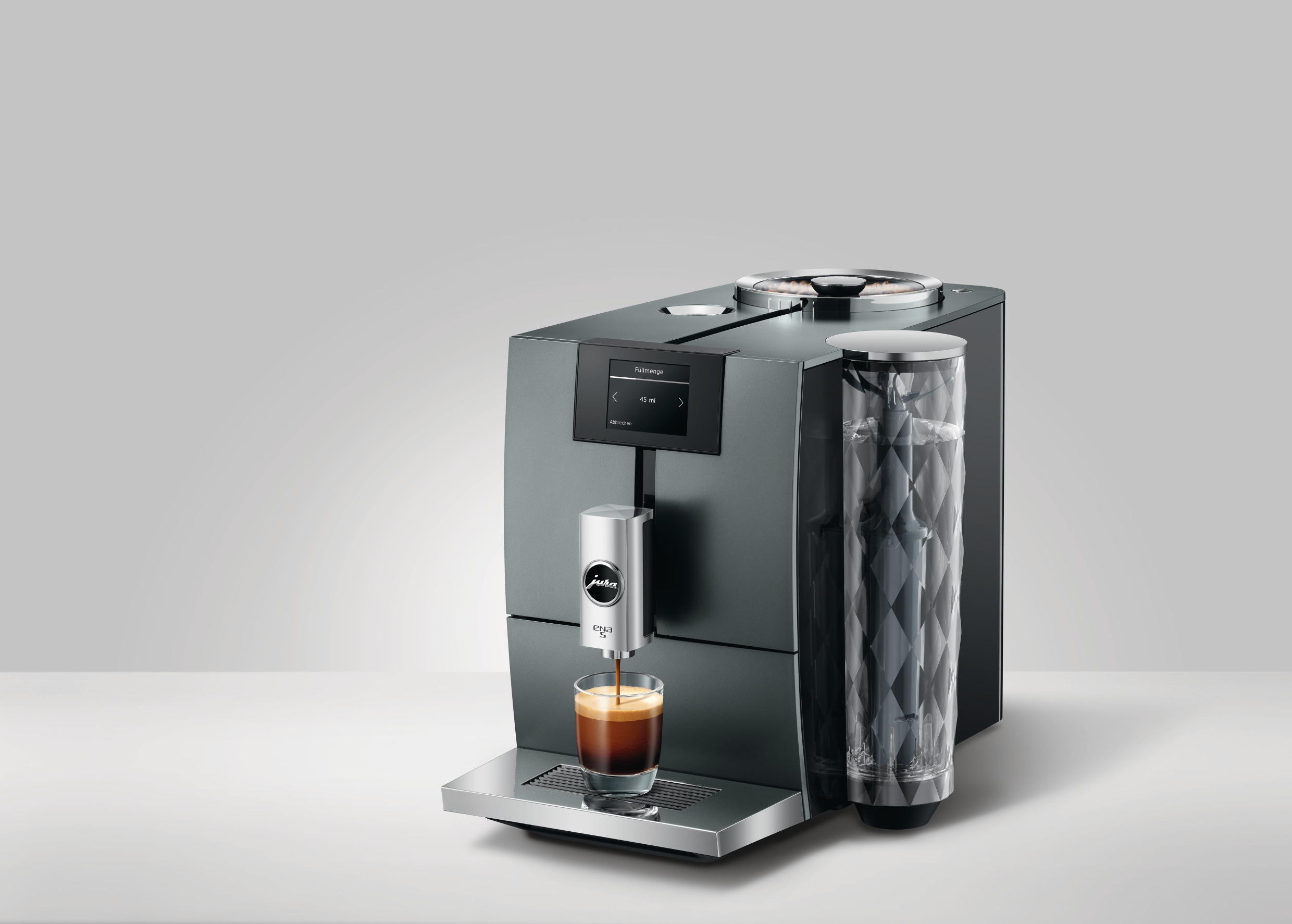 Jura ENA 8 Kaffeemaschine, dunkelgrau, mit einem Glas Espresso, schräge Ansicht.