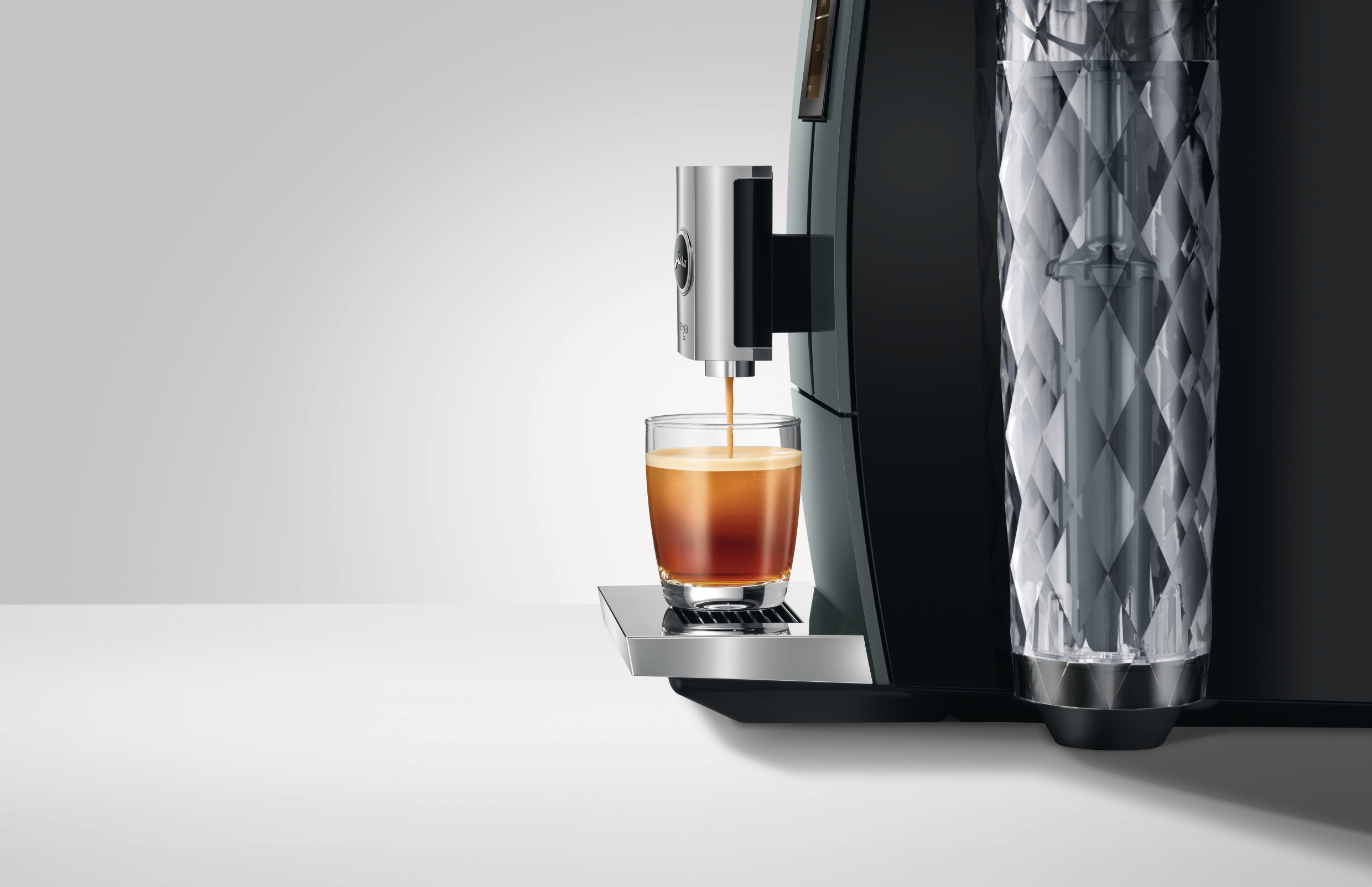 Kaffeemaschine gibt Espresso in ein klares Glas aus. Maschine ist schwarz und Stahl.