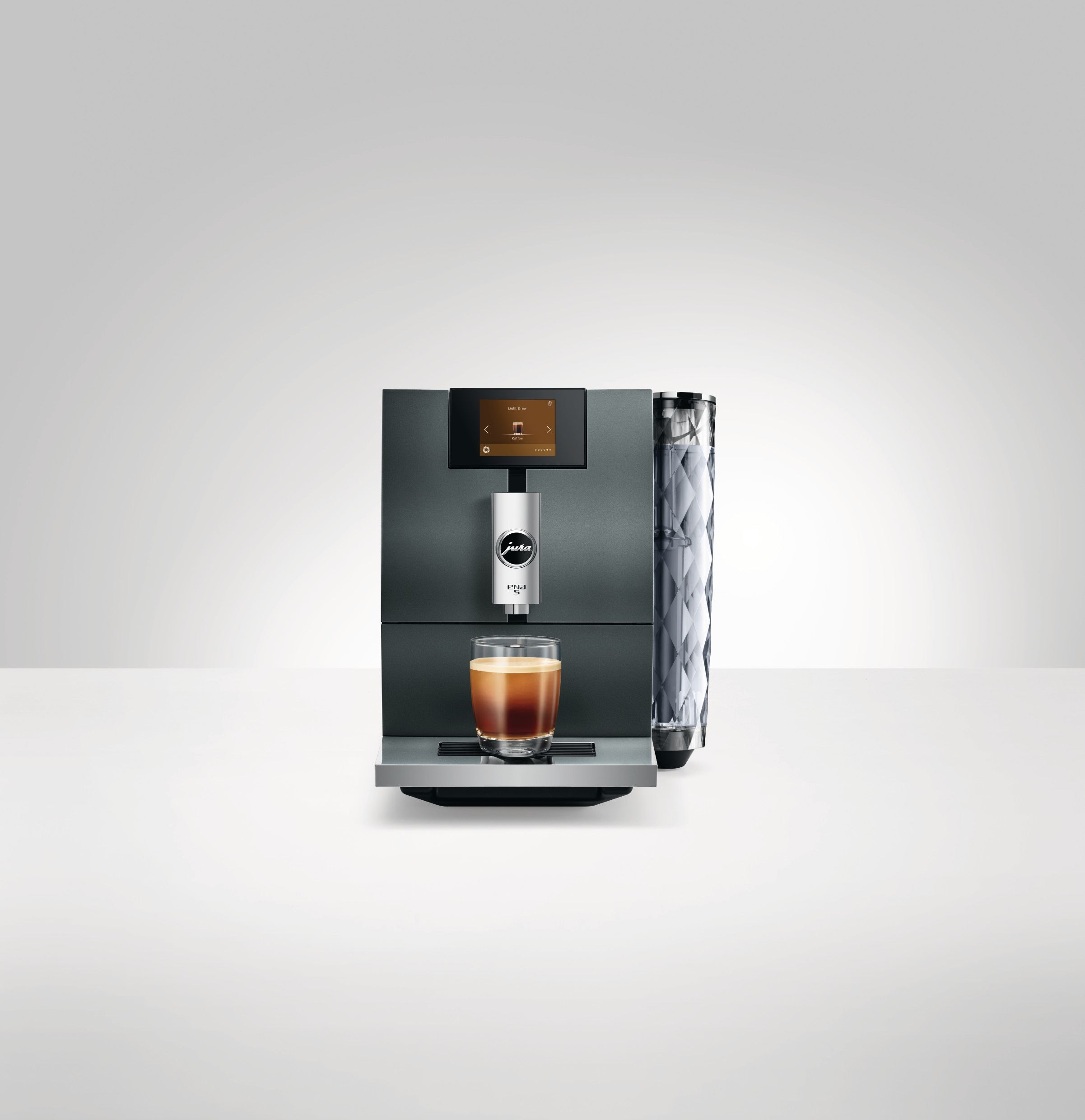 Eine dunkelgraue Kaffeemaschine mit einem Glas Kaffee davor. Weißer Hintergrund.