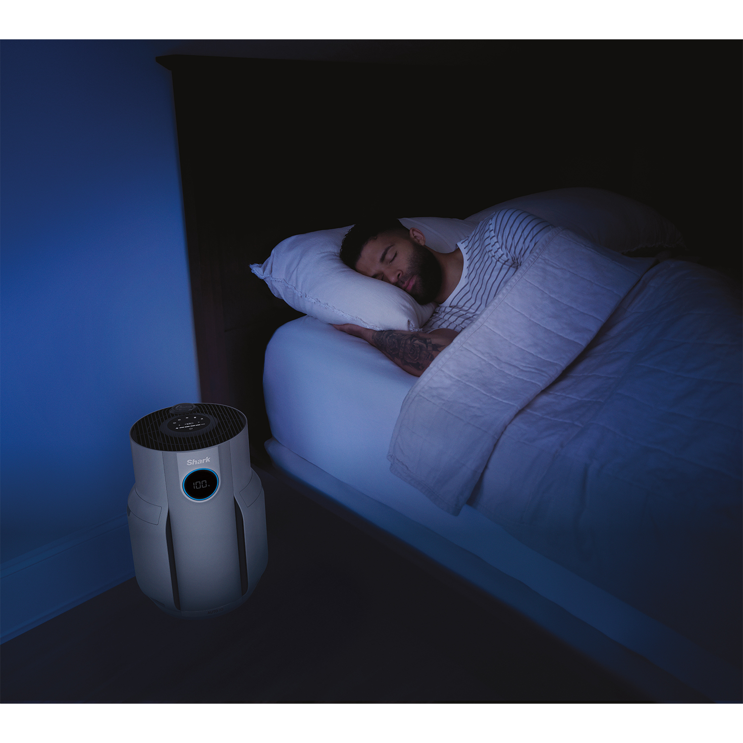 Un uomo dorme a letto vicino a un purificatore d'aria. La stanza è buia con una luce blu.