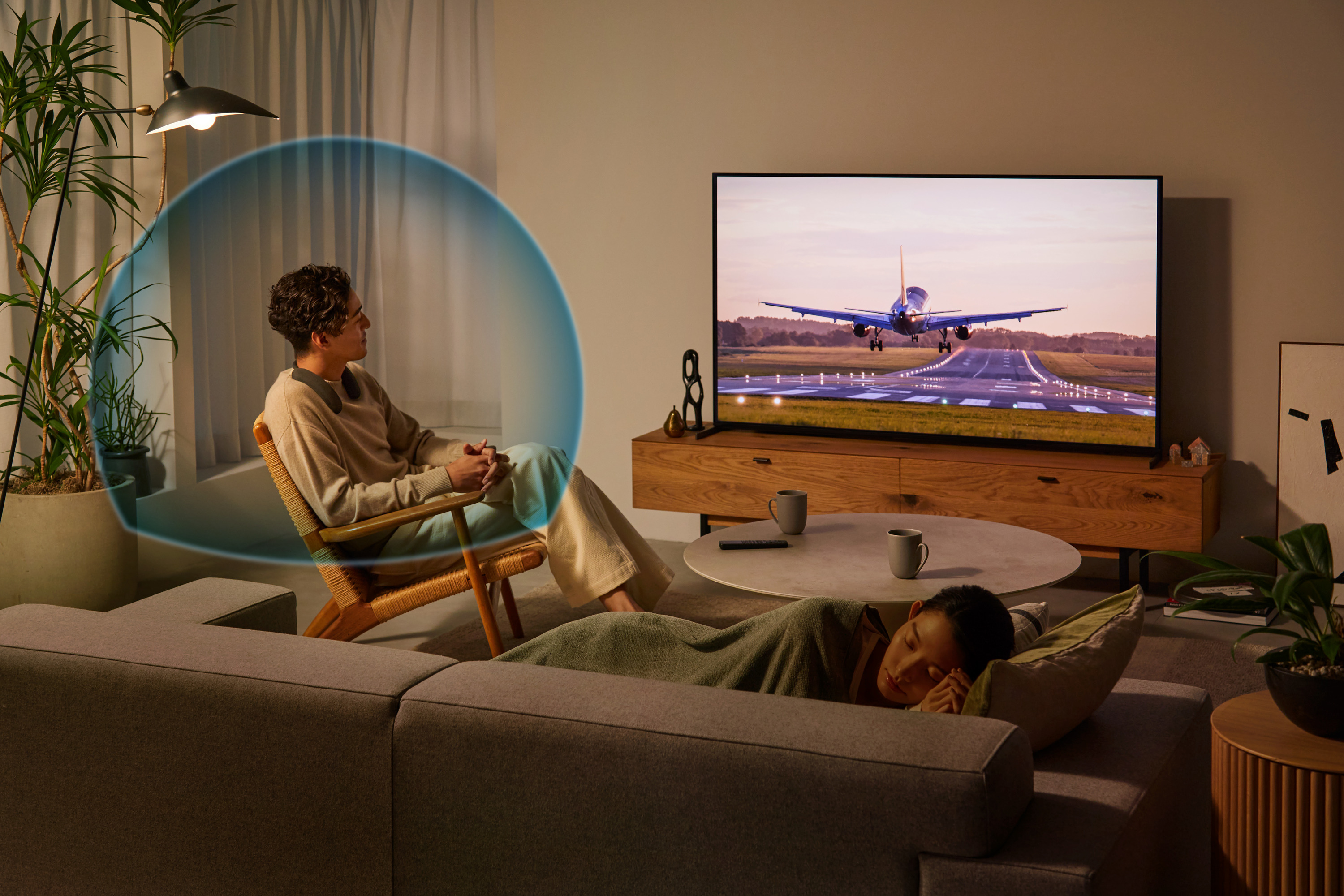 Scène de salon. Un homme assis sur une chaise, une femme dormant sur le canapé et une TV.