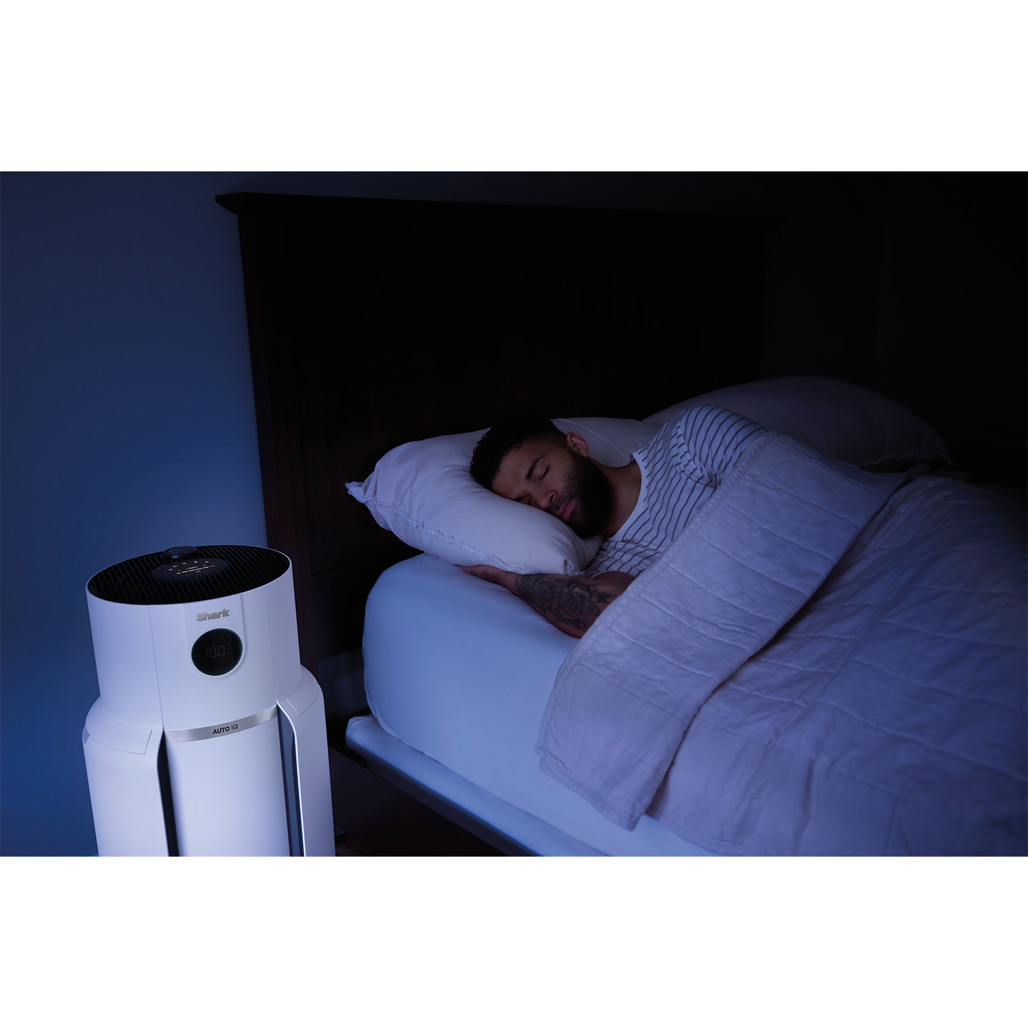 Uomo che dorme a letto con un purificatore d'aria bianco.
