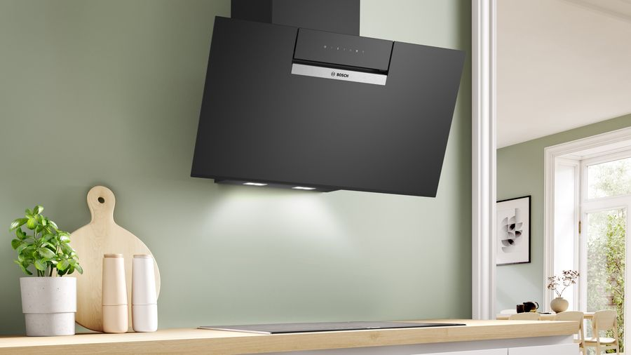 Campana extractora negra montada en pared verde claro, con encimera de madera debajo.