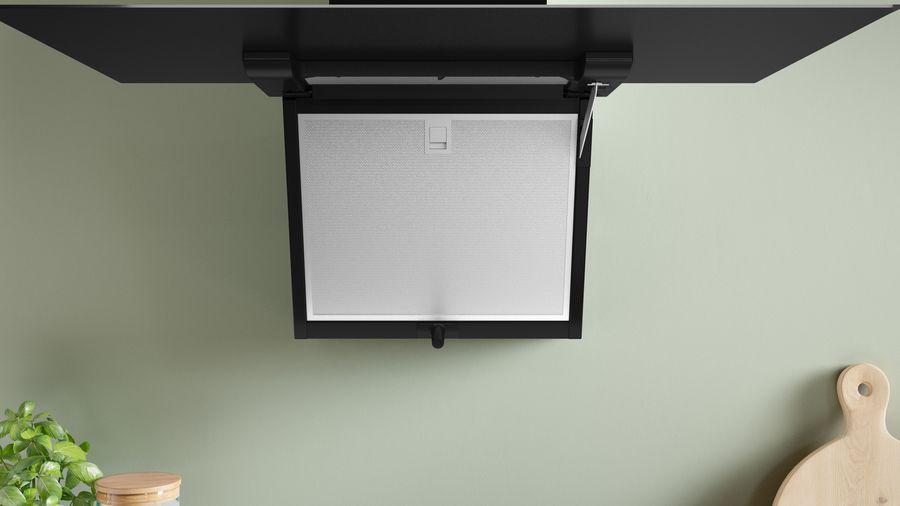Una campana extractora negra, con filtro blanco y techo negro sobre pared verde.