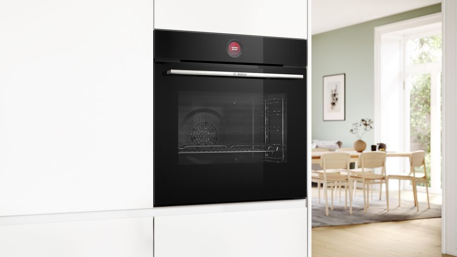 Un horno negro instalado en una cocina blanca. La puerta del horno está abierta, y la luz entra.