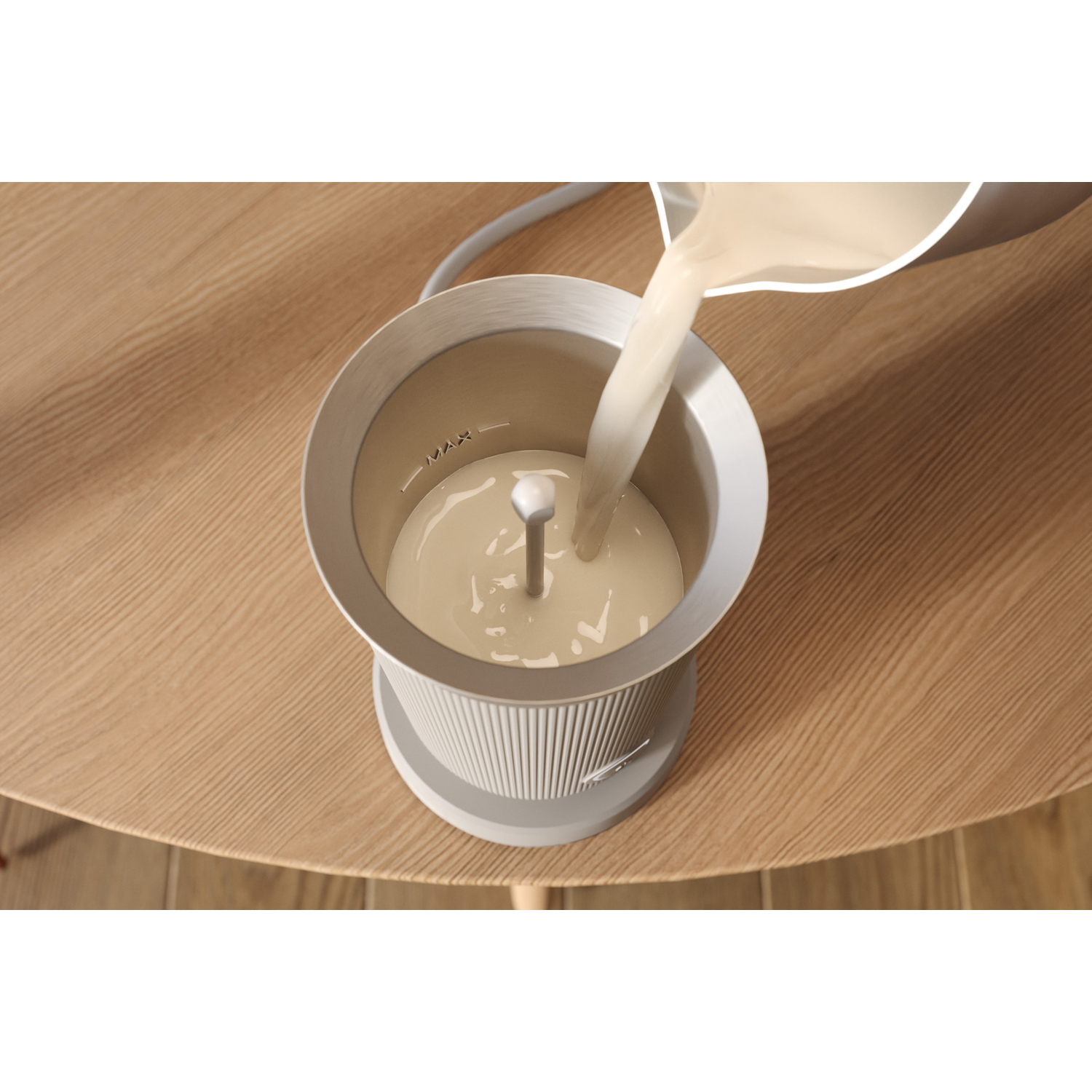 Milk pouring into a white and grey frother on a wooden table.