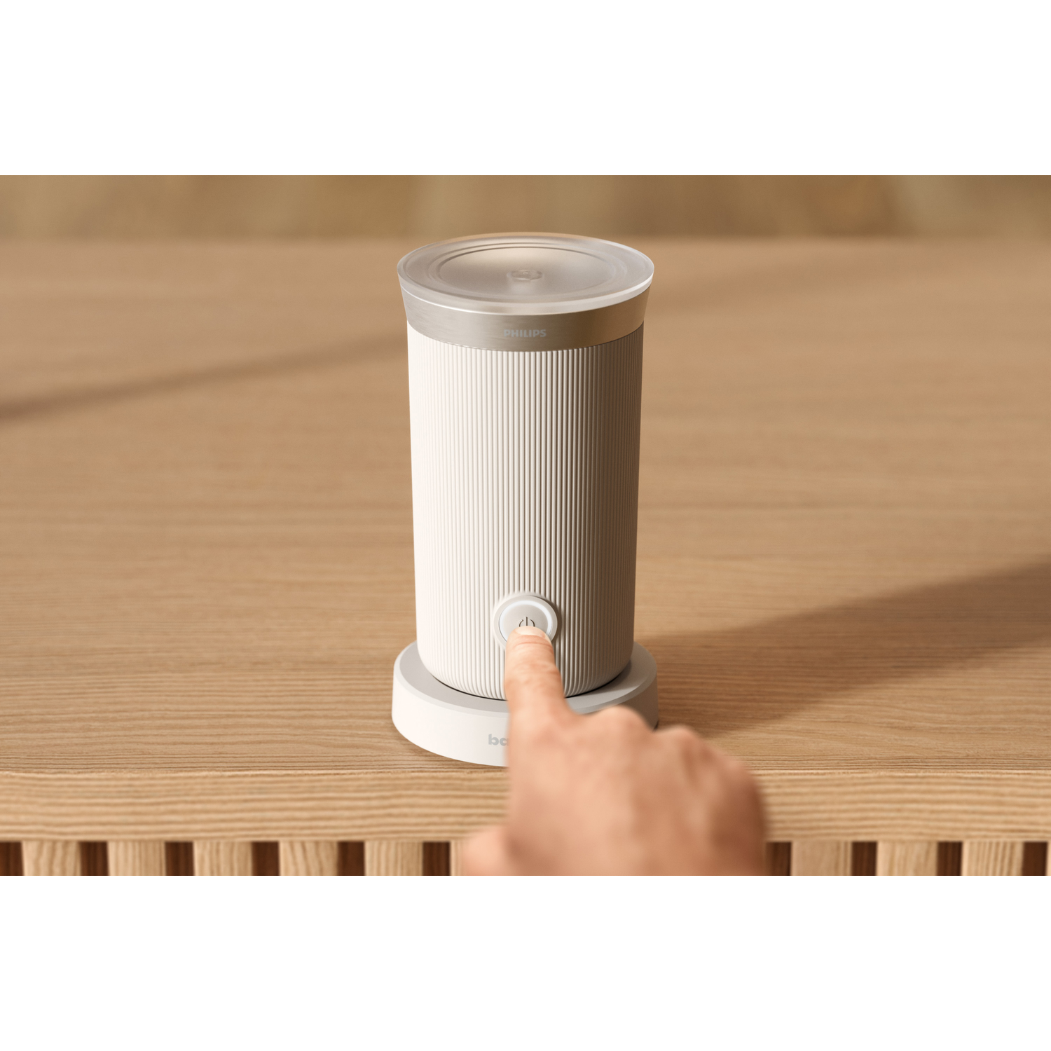 Person's finger presses power button on a cylindrical white speaker on a wooden surface.