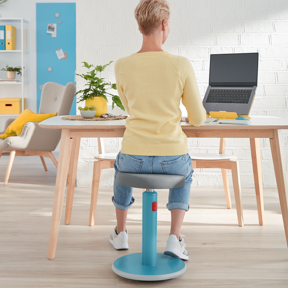Nő laptopon dolgozik, egy türkiz ergonomikus széken ülve.