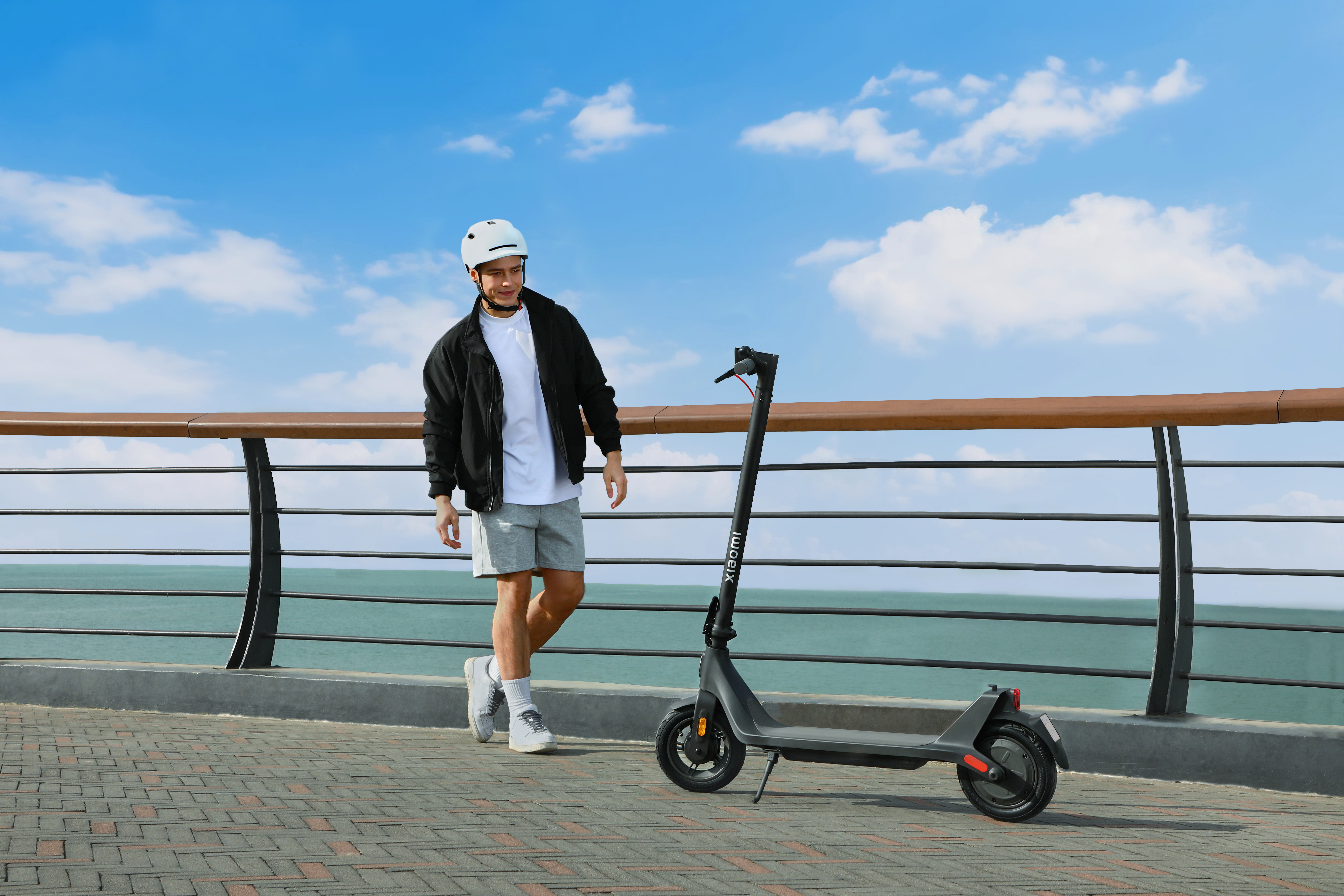 Ein Mann in Shorts und Jacke geht an einem sonnigen Tag in der Nähe eines Elektrorollers.