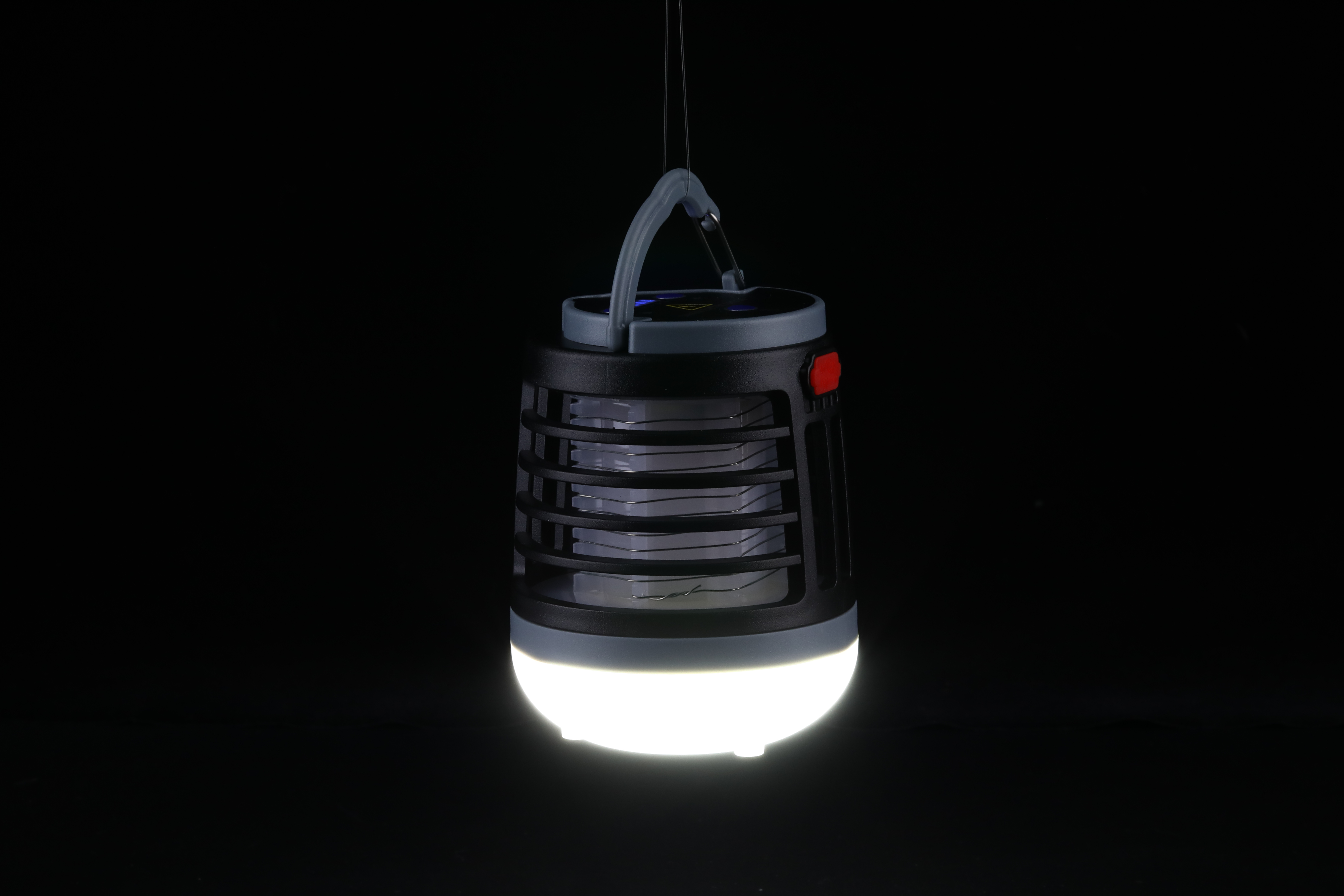 Trampa para mosquitos negra colgando en la oscuridad. Tiene una luz brillante en la parte inferior y un asa en la parte superior.