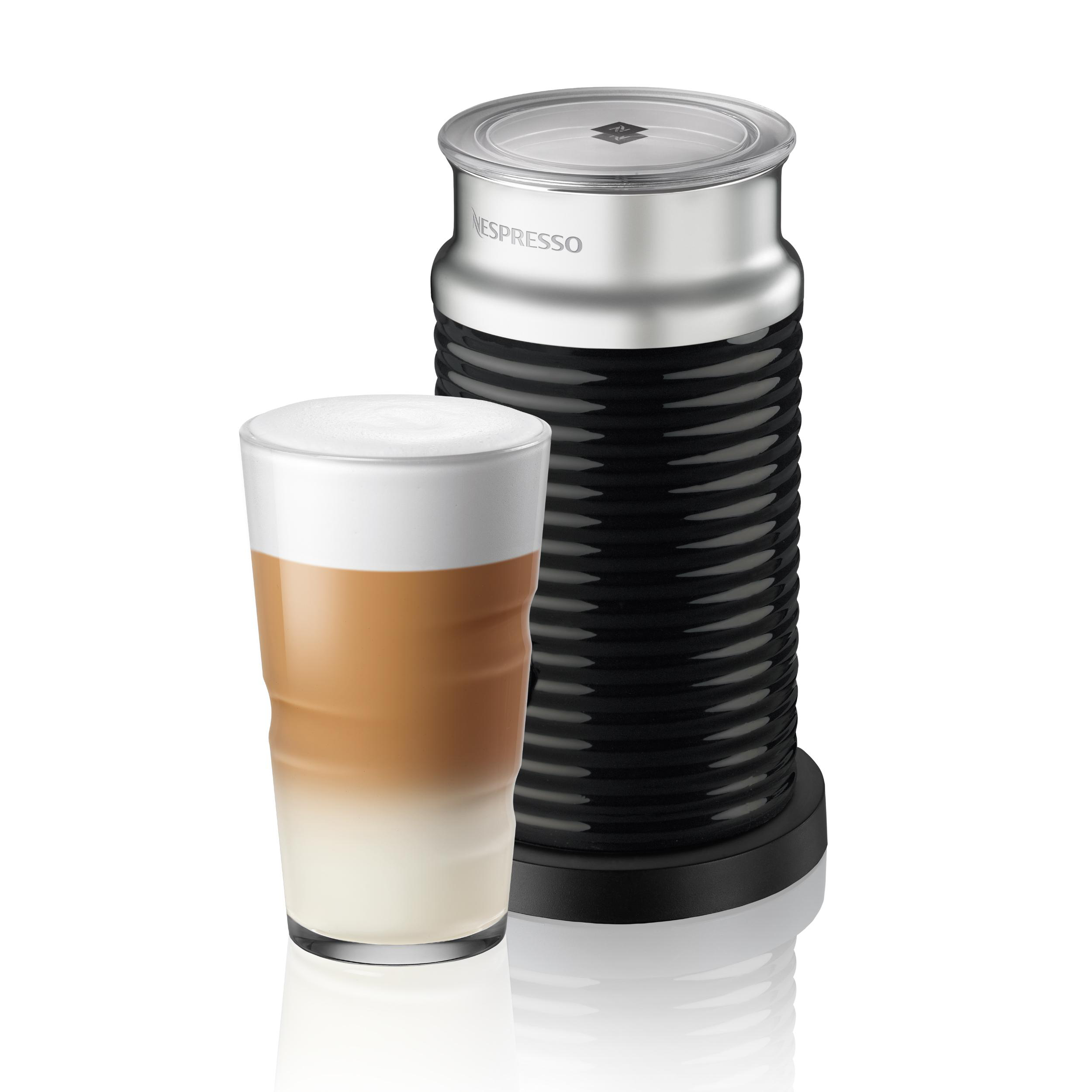 Nespresso Milchaufschäumer und ein Glas Latte Macchiato auf weißer Oberfläche.