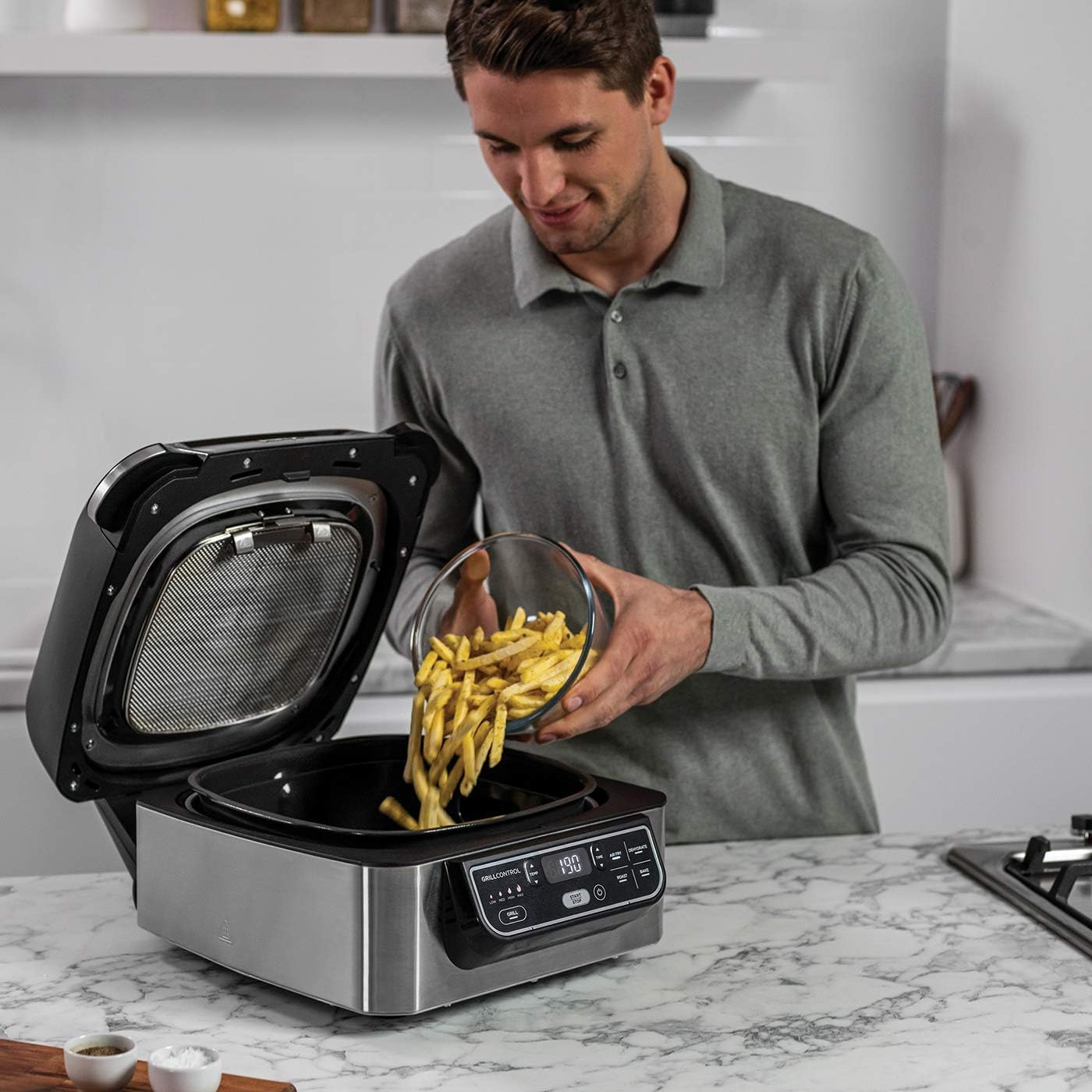 Un uomo versa patatine fritte in una friggitrice ad aria aperta, ambiente cucina.