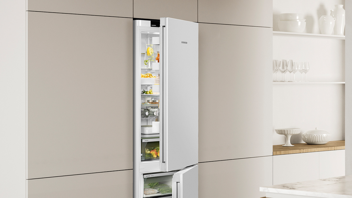 Weißer Kühlschrank, geöffnet. Innen Regale mit Essen und Getränken. Küchenhintergrund.
