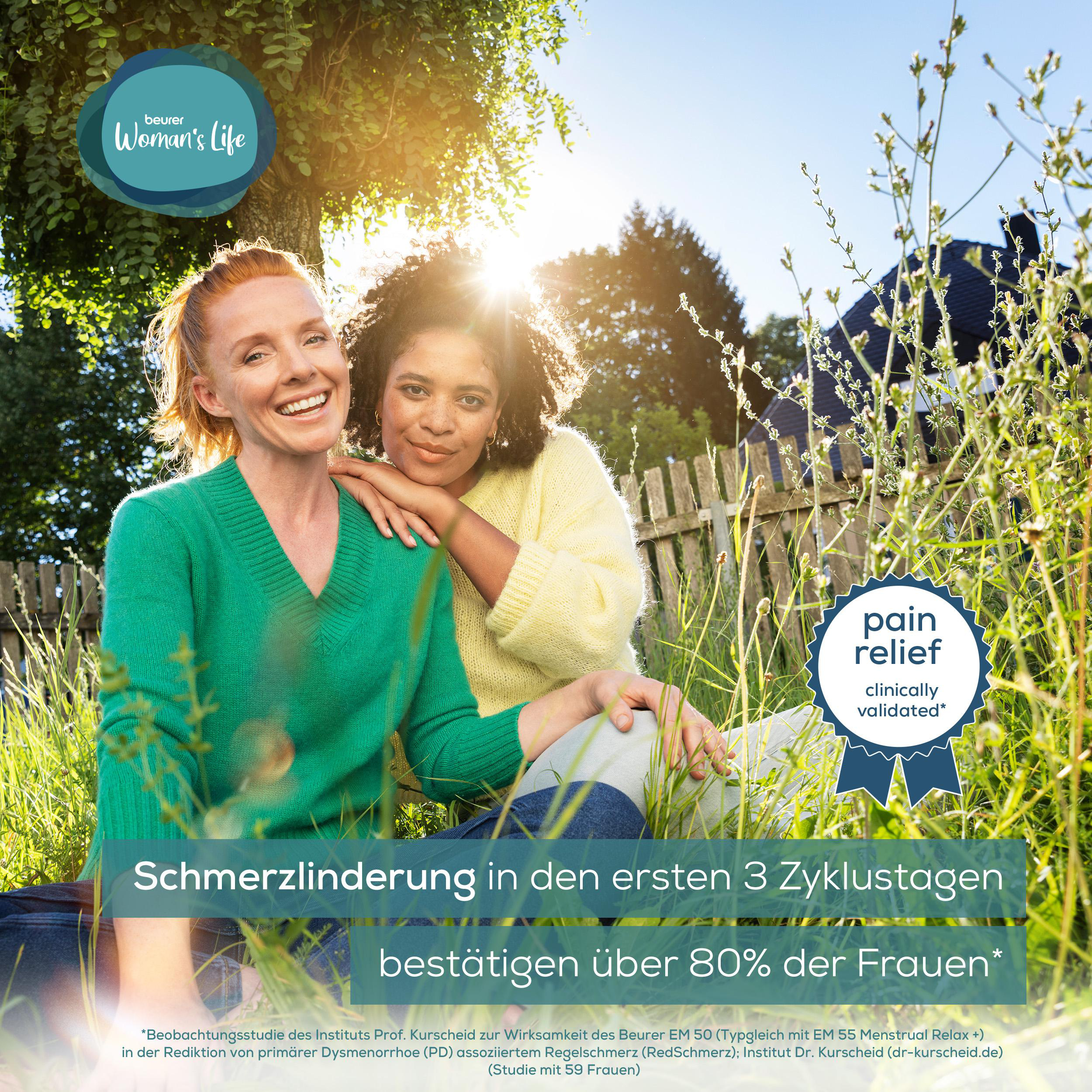 Zwei Frauen lächeln in einem Garten. Eine hat einen grünen Pullover, die andere gelb. Text-Overlay sagt: