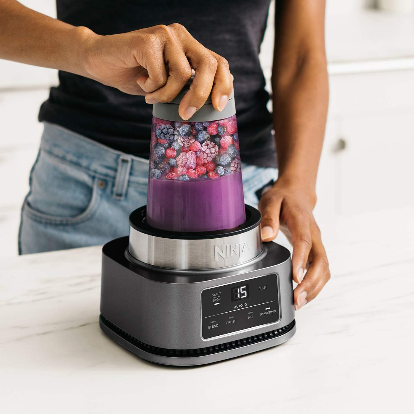 Person mixt Smoothie mit Ninja Mixer mit lila Flüssigkeit und gefrorenen Früchten.